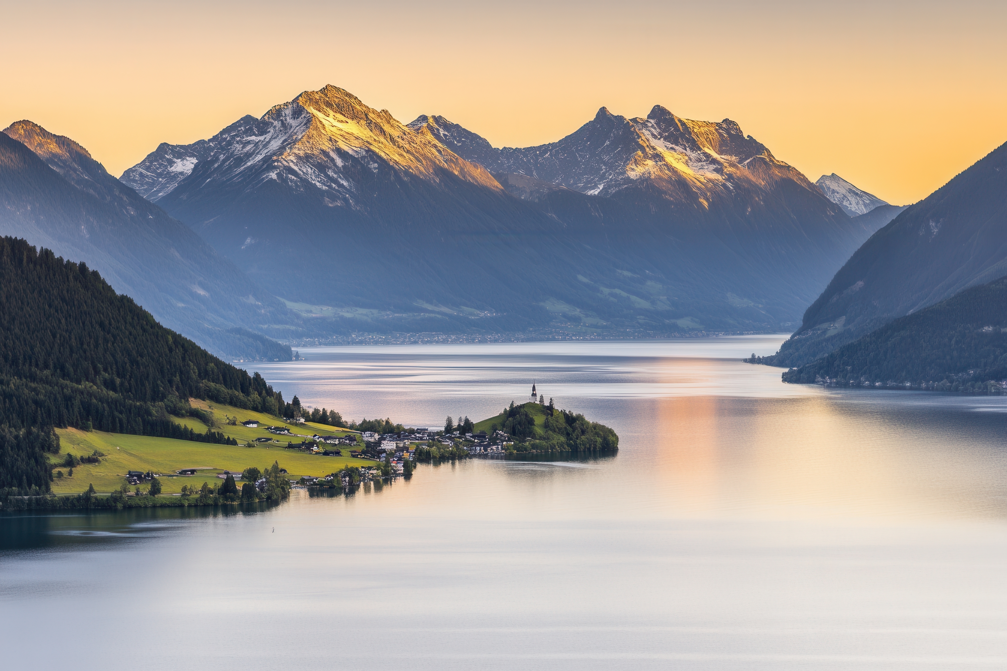 Fantastisk udsigt over den norditalienske Iseo-sø ved solnedgang med snedækkede alpetoppe, stille vand og en hyggelig landsby omgivet af grønne skove