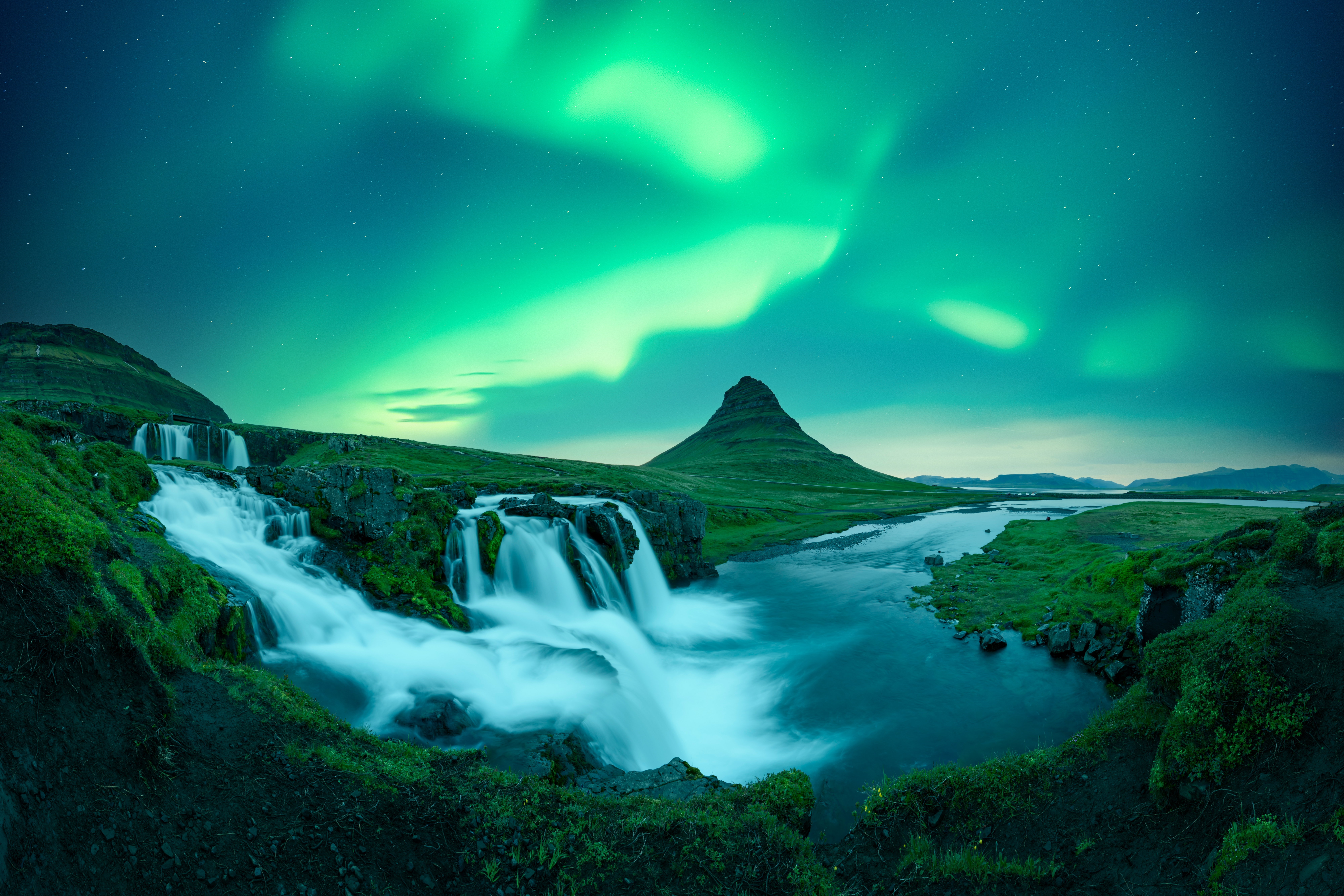 Fantastisk islandsk natscene med det dramatiske nordlys, der danner en grøn himmel over Kirkjufellsfoss-vandfaldet og det kegleformede Kirkjufell-bjerg