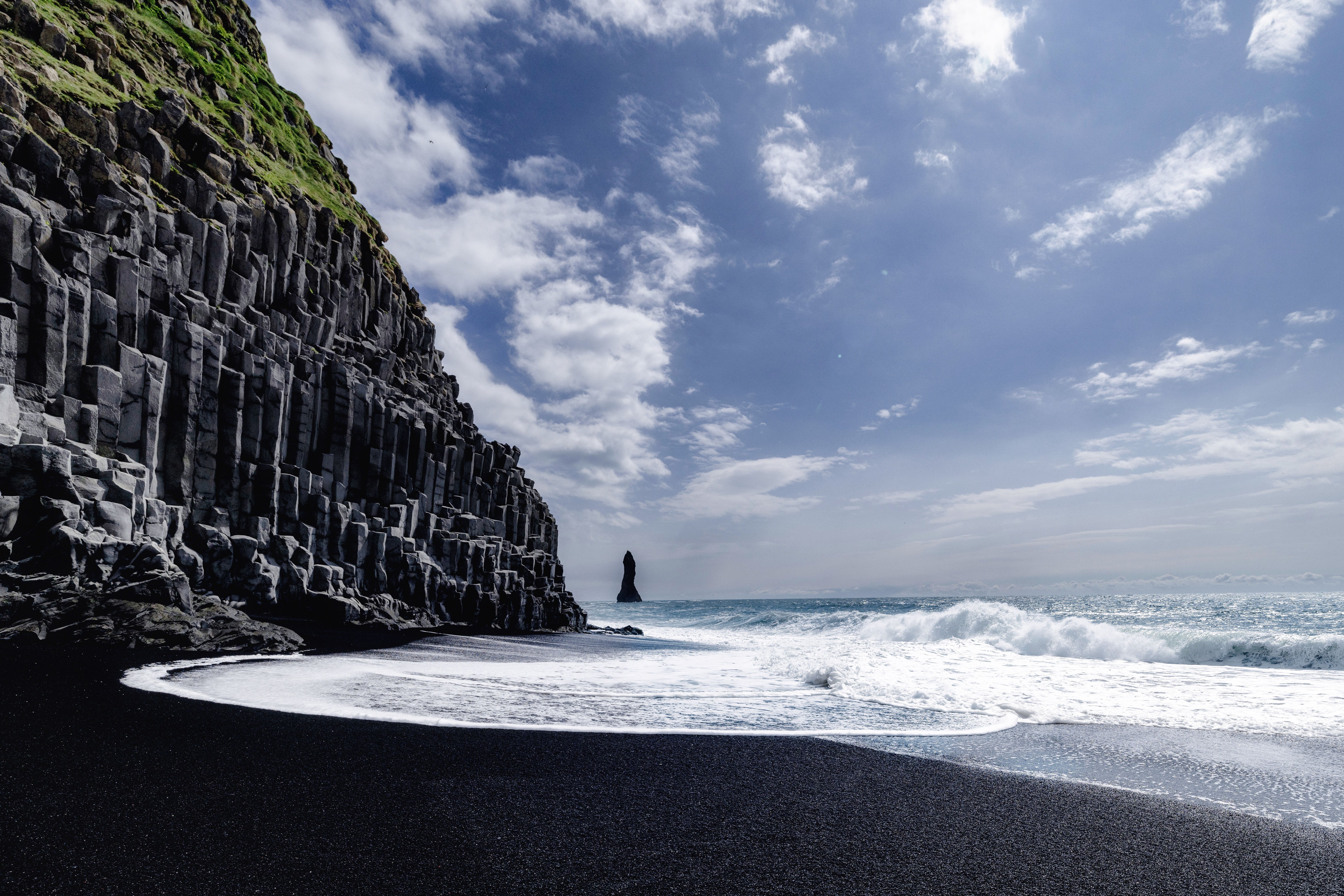 Spektakulær udsigt over Reynisfjara sort sandstrand med geologiske basaltsøjler og dramatiske havbølger på Island
