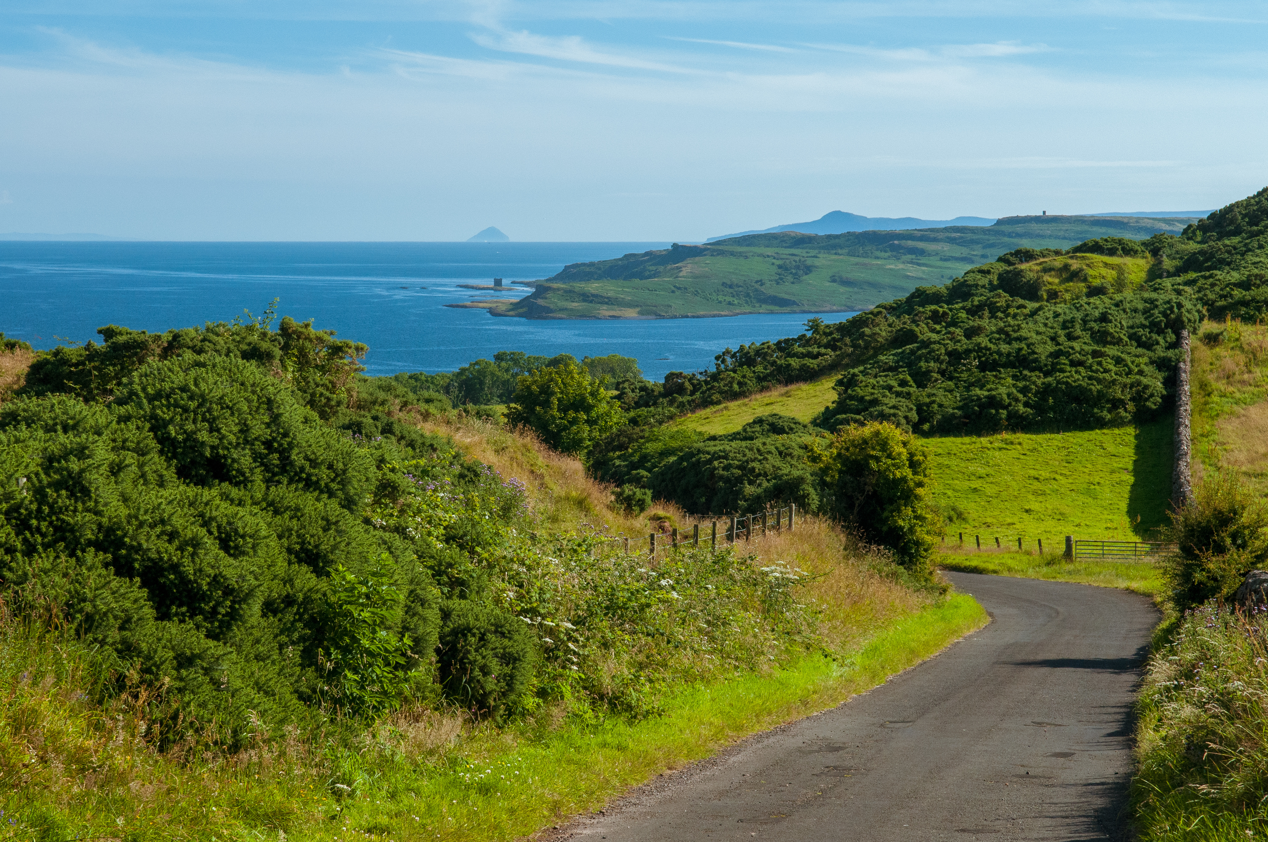 Naturskøn kystvej på Isle of Arran i Skotland omgivet af grøn vegetation og med panoramaudsigt over havet og Ailsa Craig