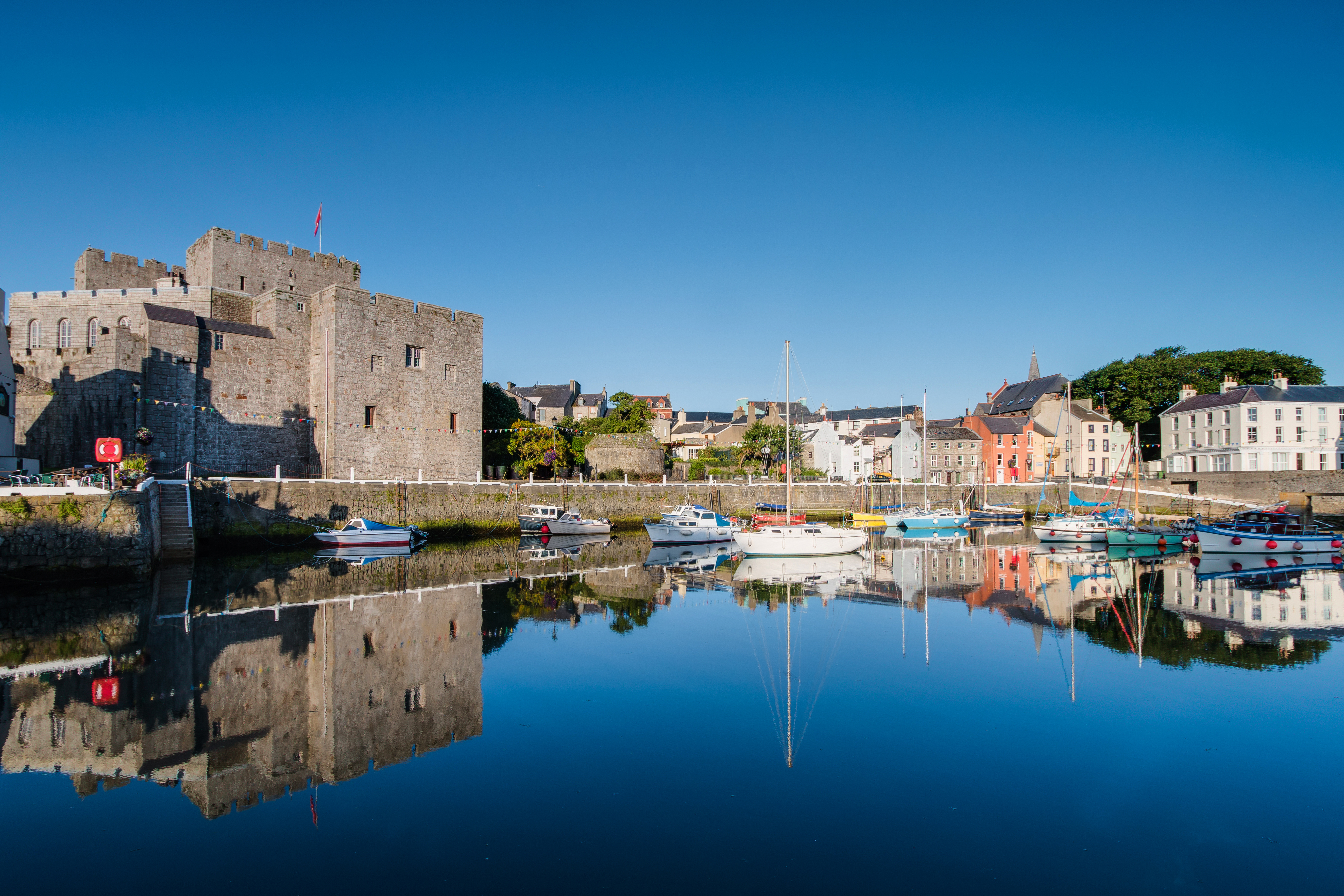 Idyllisk havnescene med Castle Rushen og sejlbåde i Castletown på Isle of Man med perfekte vandrefleksioner