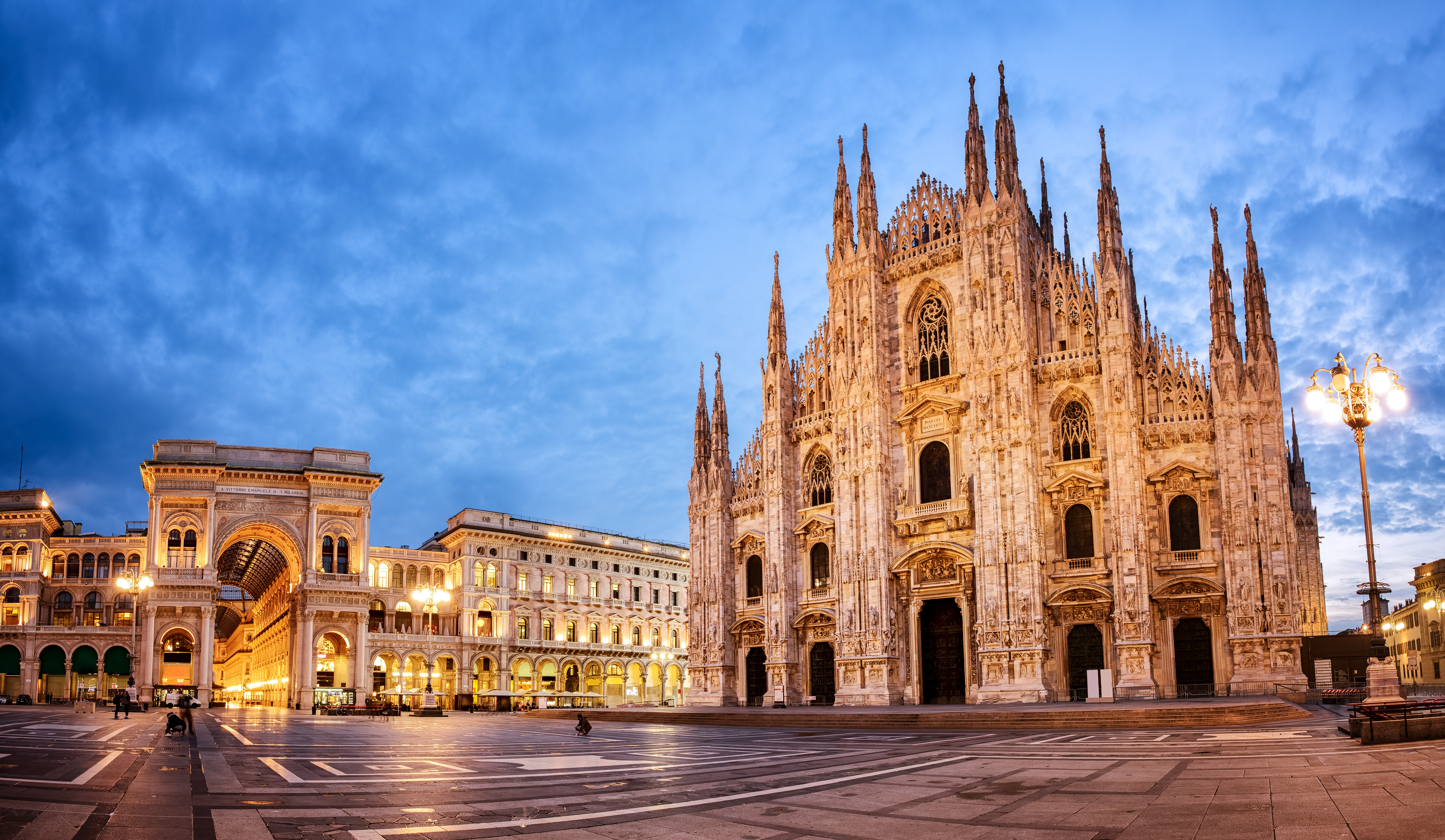 Fascinerende natbillede af den berømte Milano Domkirke med dens karakteristiske hvide marmorfacade, talrige spir og gotiske detaljer, der har gjort den til et af Italiens mest besøgte arkitektoniske mesterværker