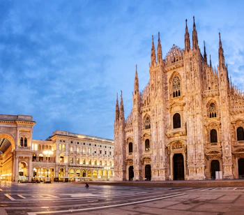 Fascinerende natbillede af den berømte Milano Domkirke med dens karakteristiske hvide marmorfacade, talrige spir og gotiske detaljer, der har gjort den til et af Italiens mest besøgte arkitektoniske mesterværker