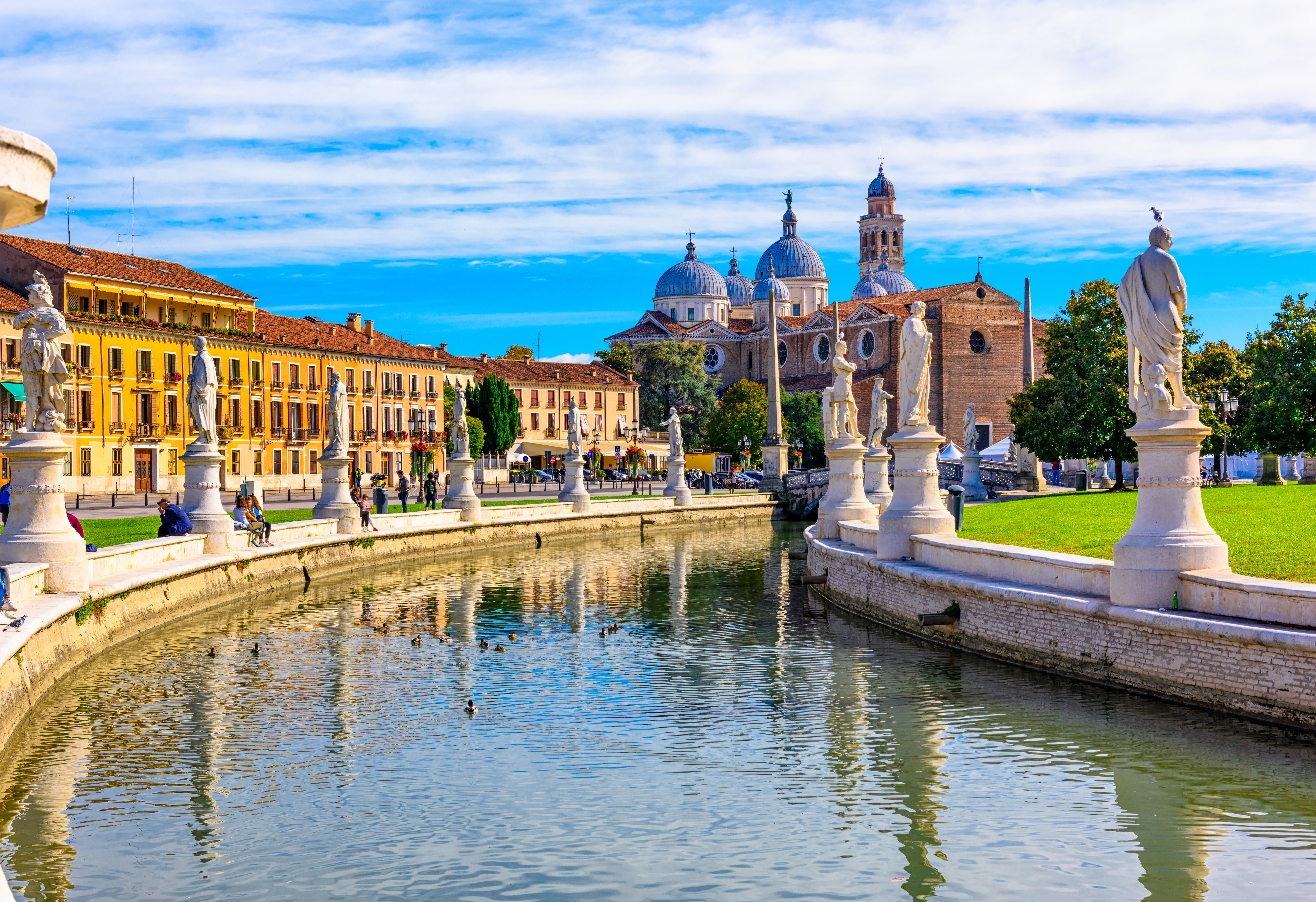 Idyllisk udsigt over den historiske Prato della Valle plads med dens karakteristiske kanal omgivet af statuer og den storslåede Basilica Santa Giustina i Padova, Italien