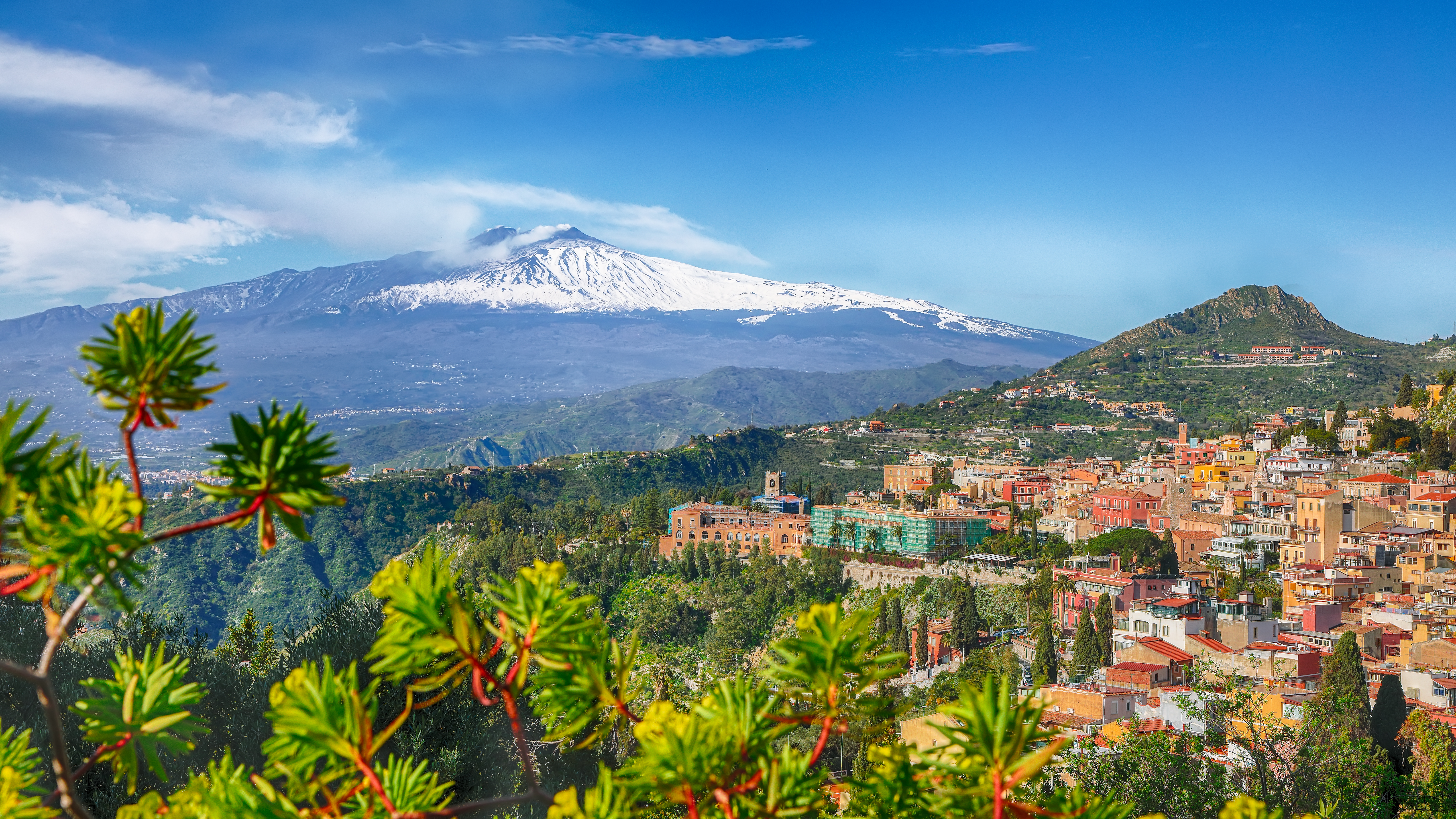 Fascinerende panoramaudsigt over den maleriske by Taormina med dens mange bygninger og terrakottatage, med den snedækkede og rygende Etna-vulkan i baggrunden på Sicilien
