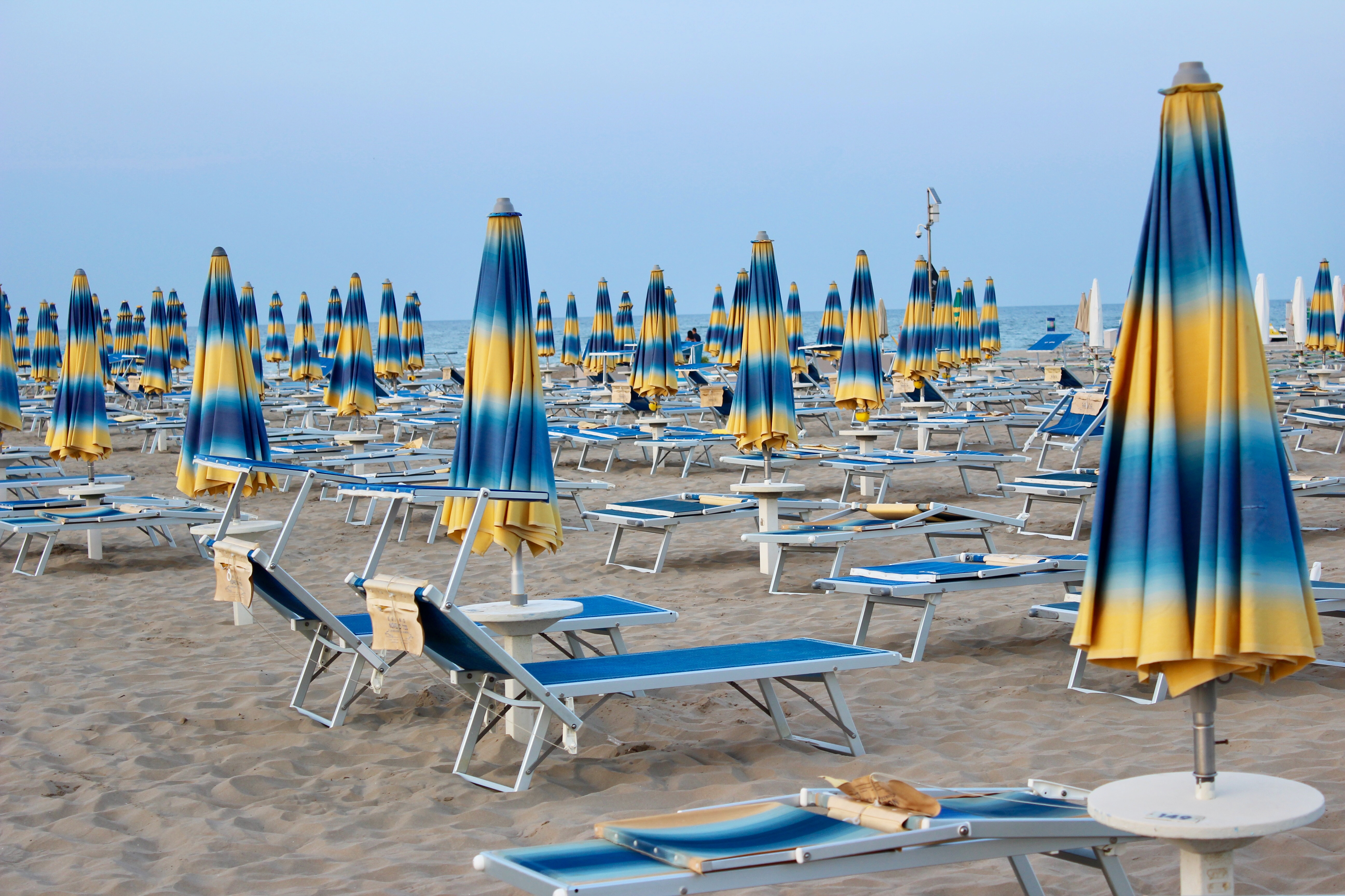 Flot italiensk badestrand med mange blå og gule parasoller og solsenge klar til afslapning
