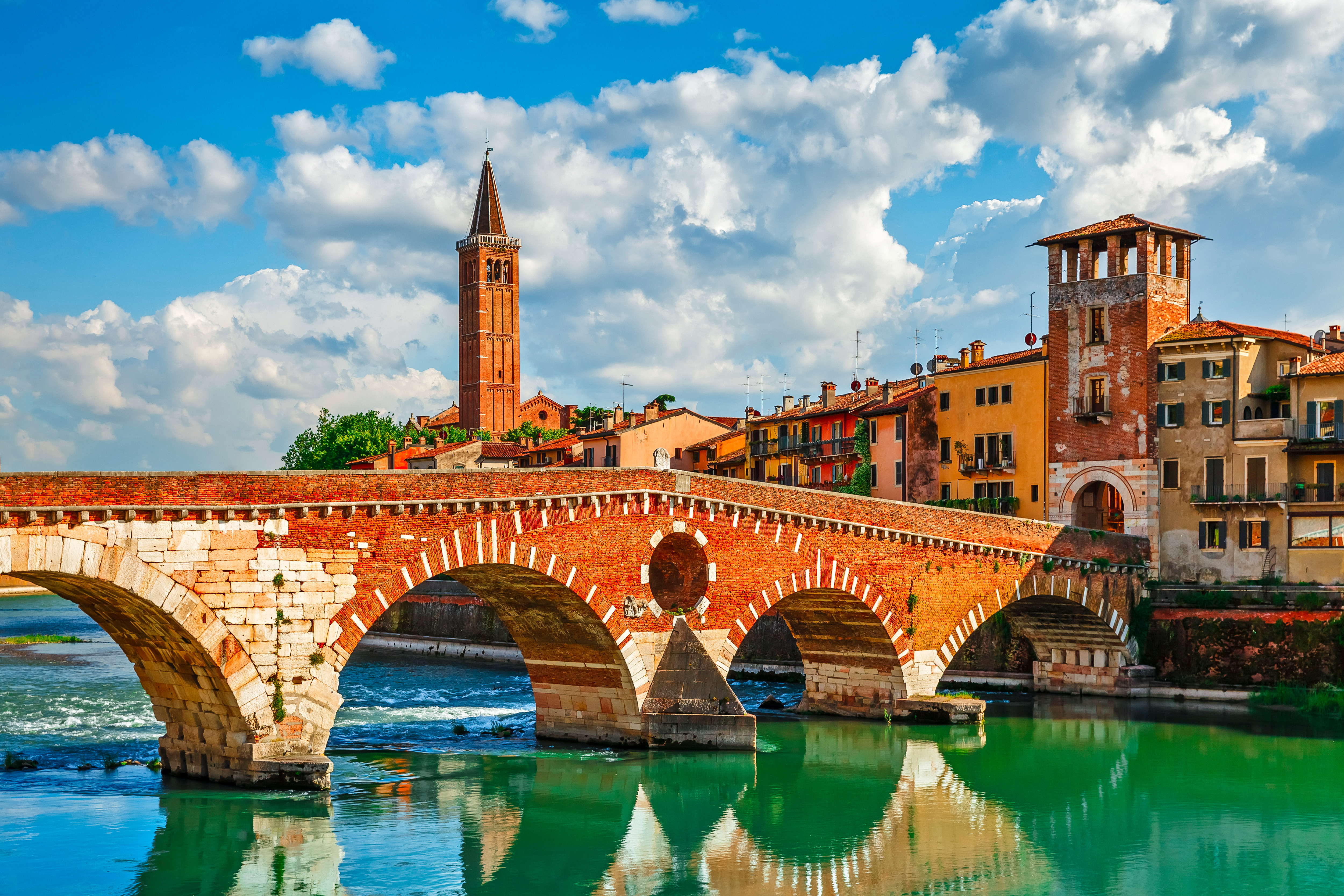 Idyllisk panorama over den antikke Ponte Pietra bro i Verona med karakteristiske terracotta-farvede bygninger og skinnende Adige-flod på en solrig dag