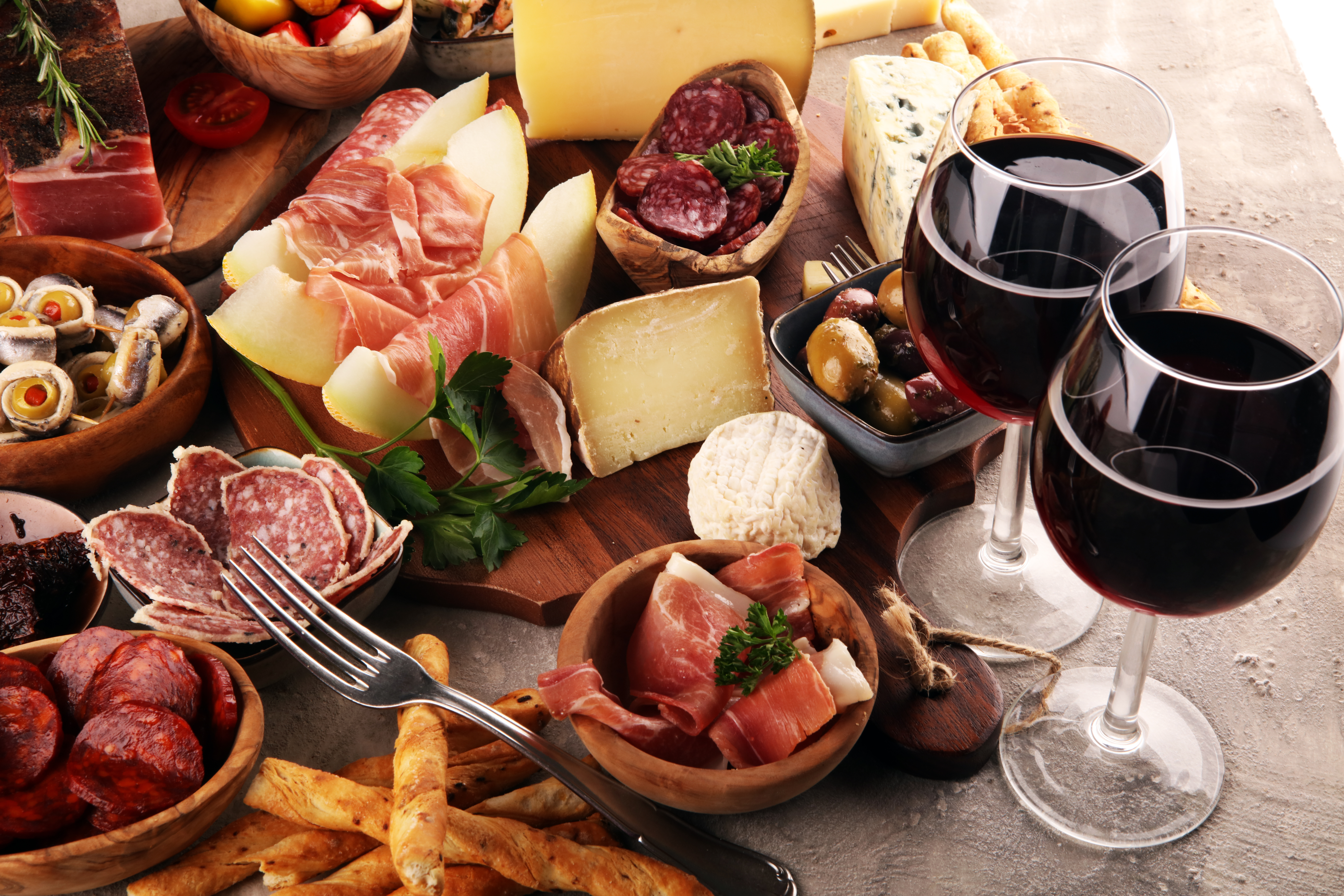 Smagfuldt italiensk antipasti-udvalg med prosciutto, salami, oste, oliven og røde vinglas på træbræt