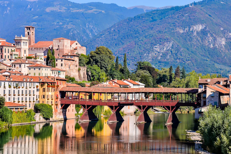 Charmerende træbro i italiensk bjerglandsby Bassano del Grappa med alpine bjerge i baggrunden