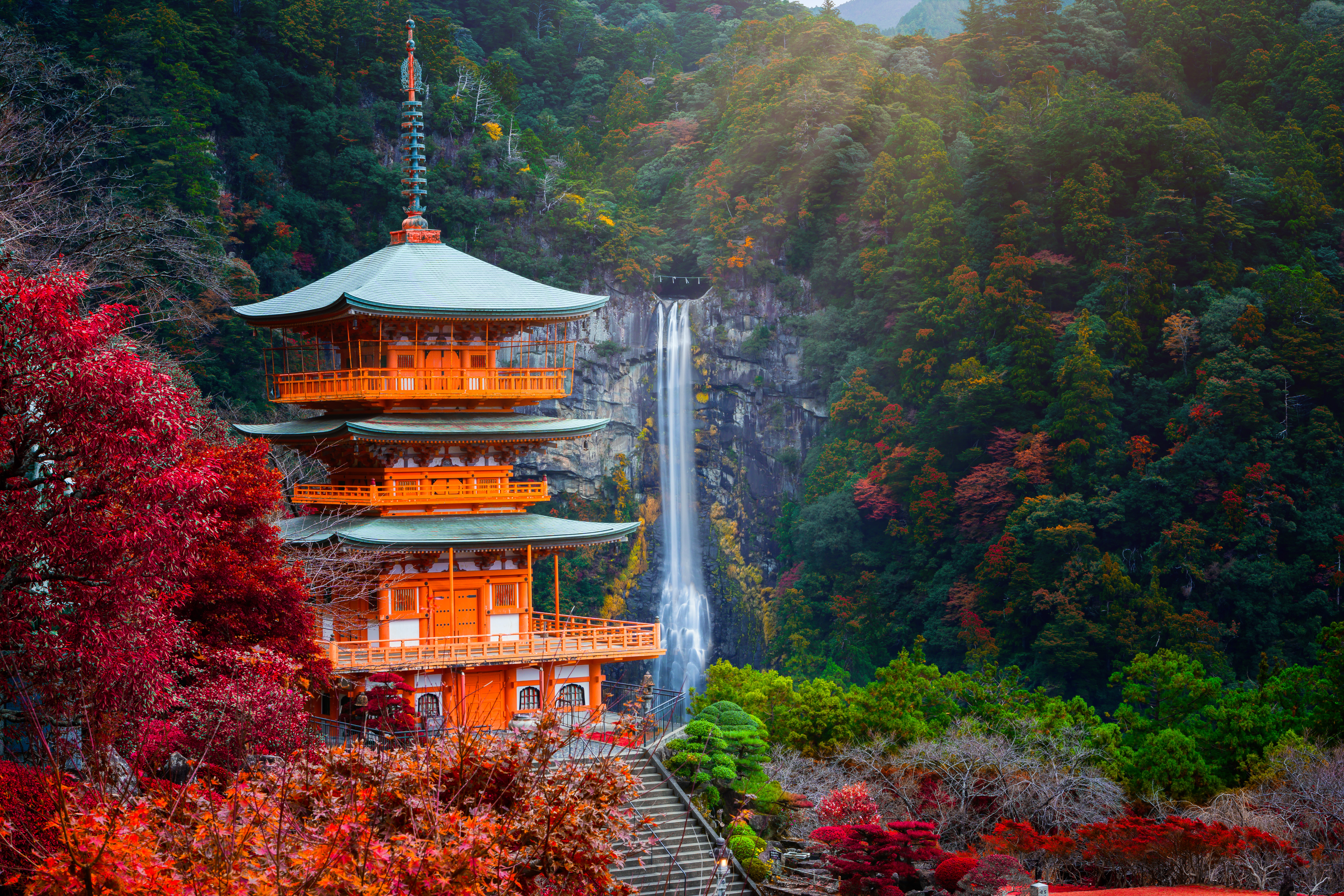 Smuk orangerød pagoda ved Kumano Nachi Taisha helligdommen med det 133 meter høje Nachi vandfald og farverig efterårsskov