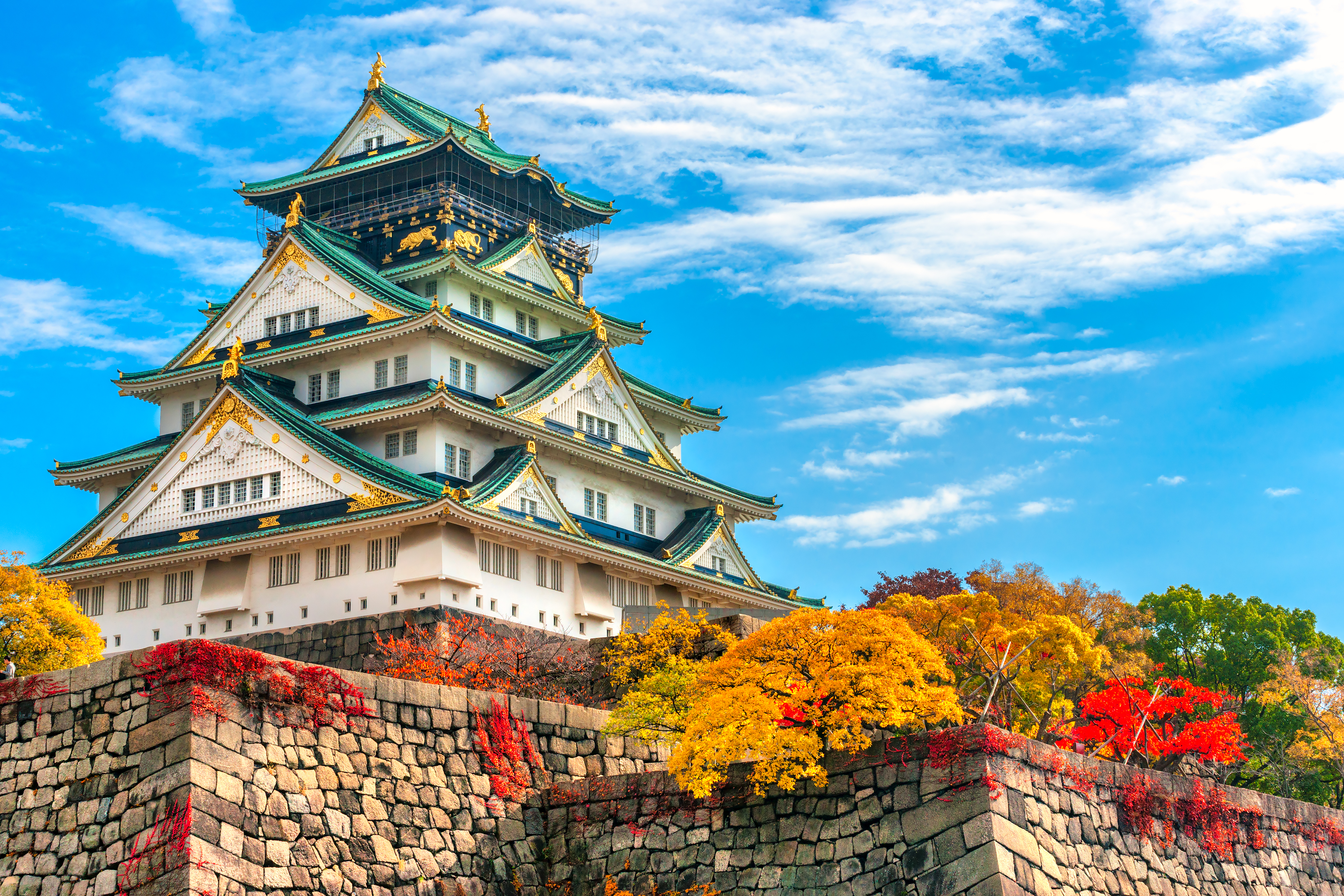 Majestaetisk Osaka Slot med roede og gule efteraarsblade under skyet himmel