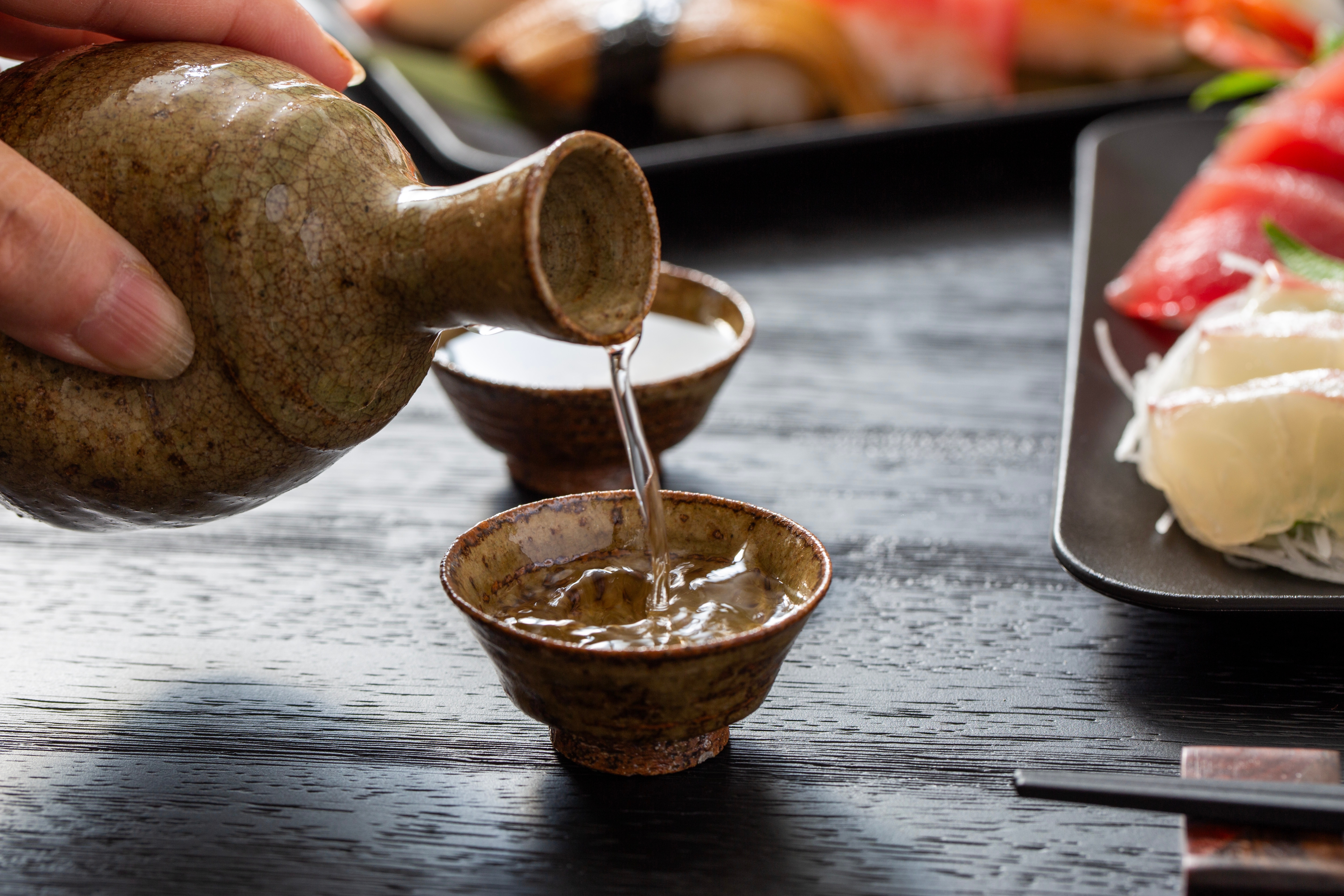 Nærbillede af sake der hældes i en keramikkop på en japansk izakaya – en autentisk smagsoplevelse fra Japans madkultur