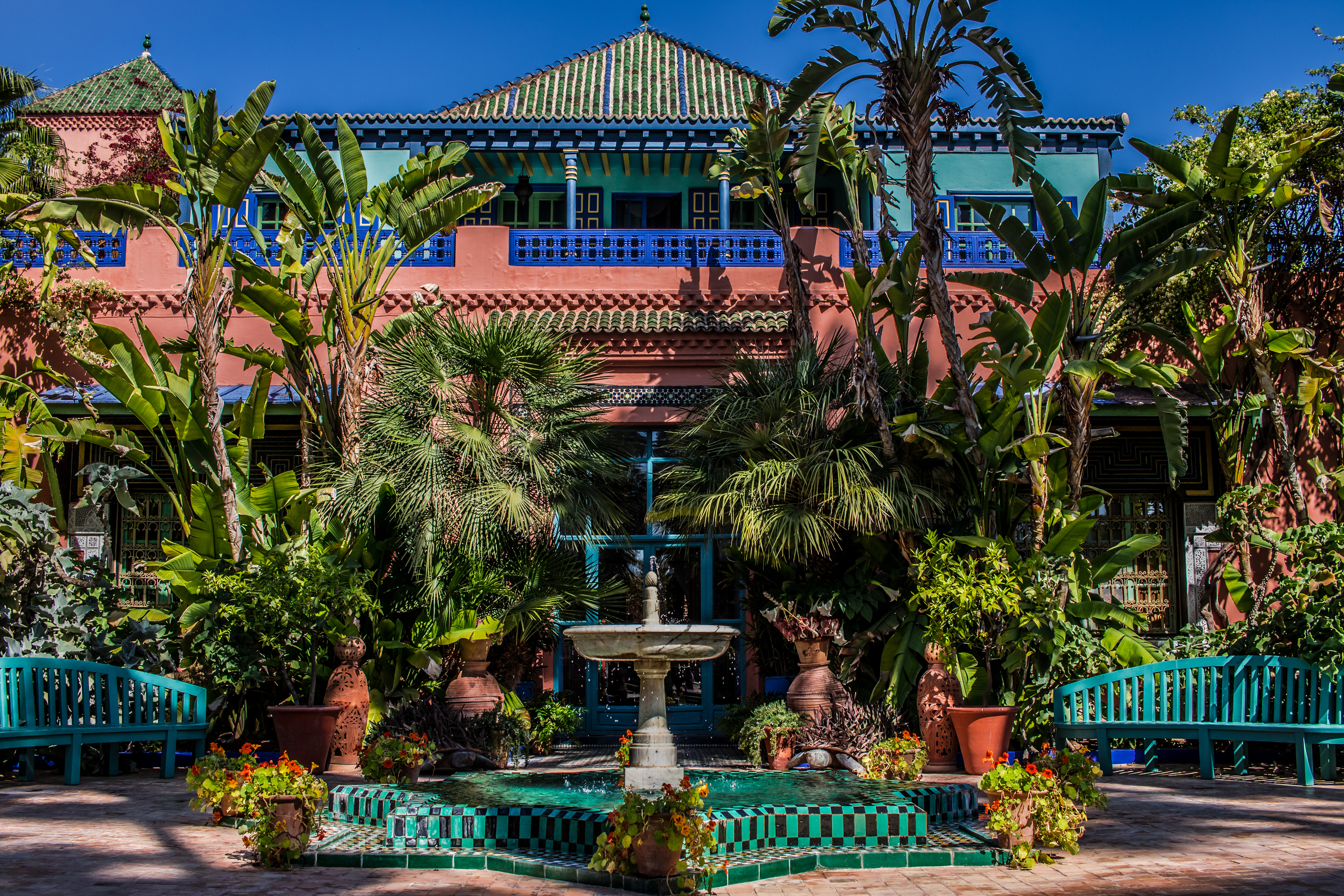 Jardin Majorelle i Marrakech med farverige bygninger, frodige tropiske planter og en dekorativ fontæne i den berømte have grundlagt af Yves Saint Laurent