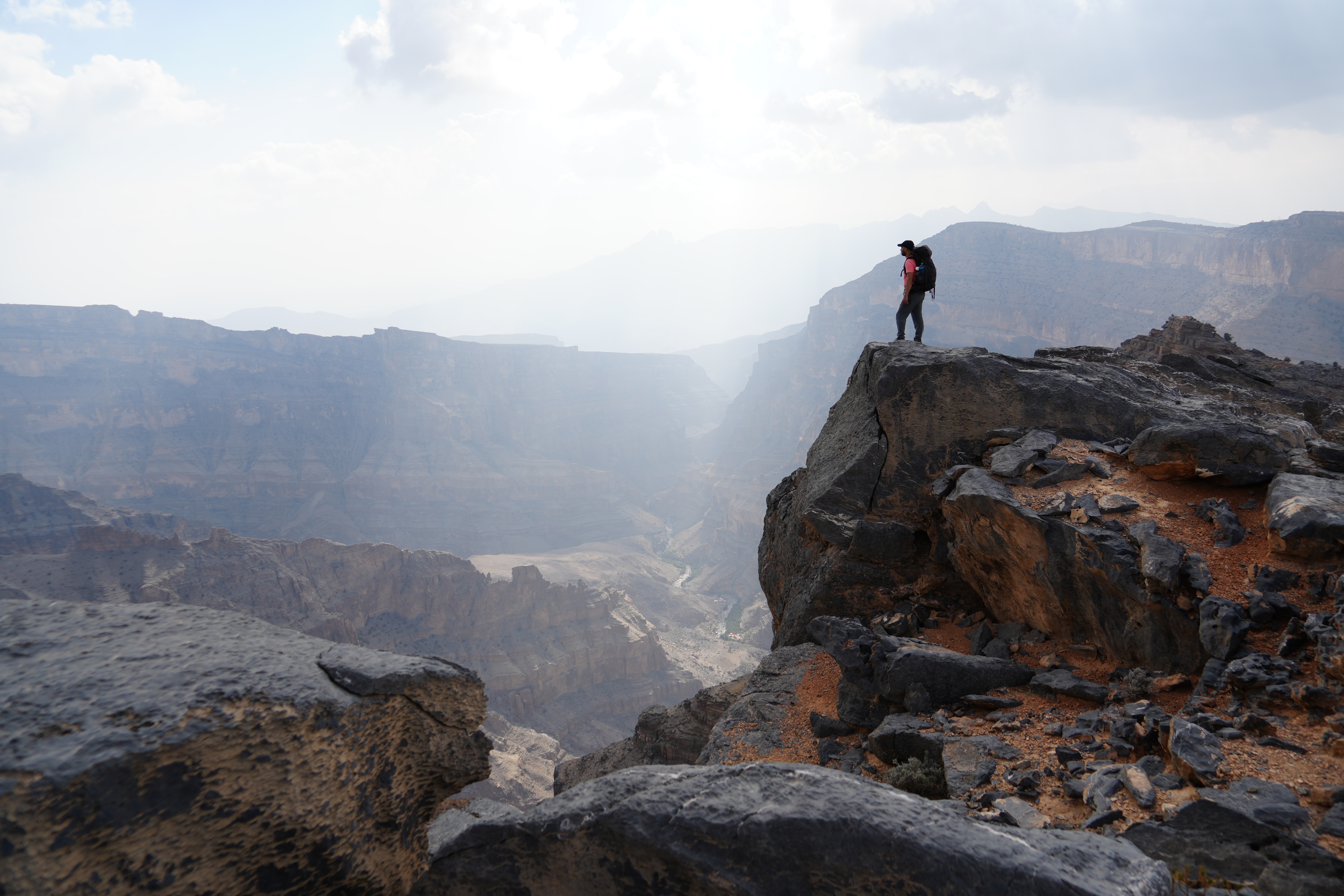 Dramatisk udsigt fra klippen ved Jebel Shams i Oman med vandrer der betragter den dybe canyon i det bjergrigt terræn