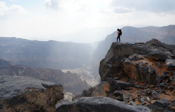 Dramatisk udsigt fra klippen ved Jebel Shams i Oman med vandrer der betragter den dybe canyon i det bjergrigt terræn