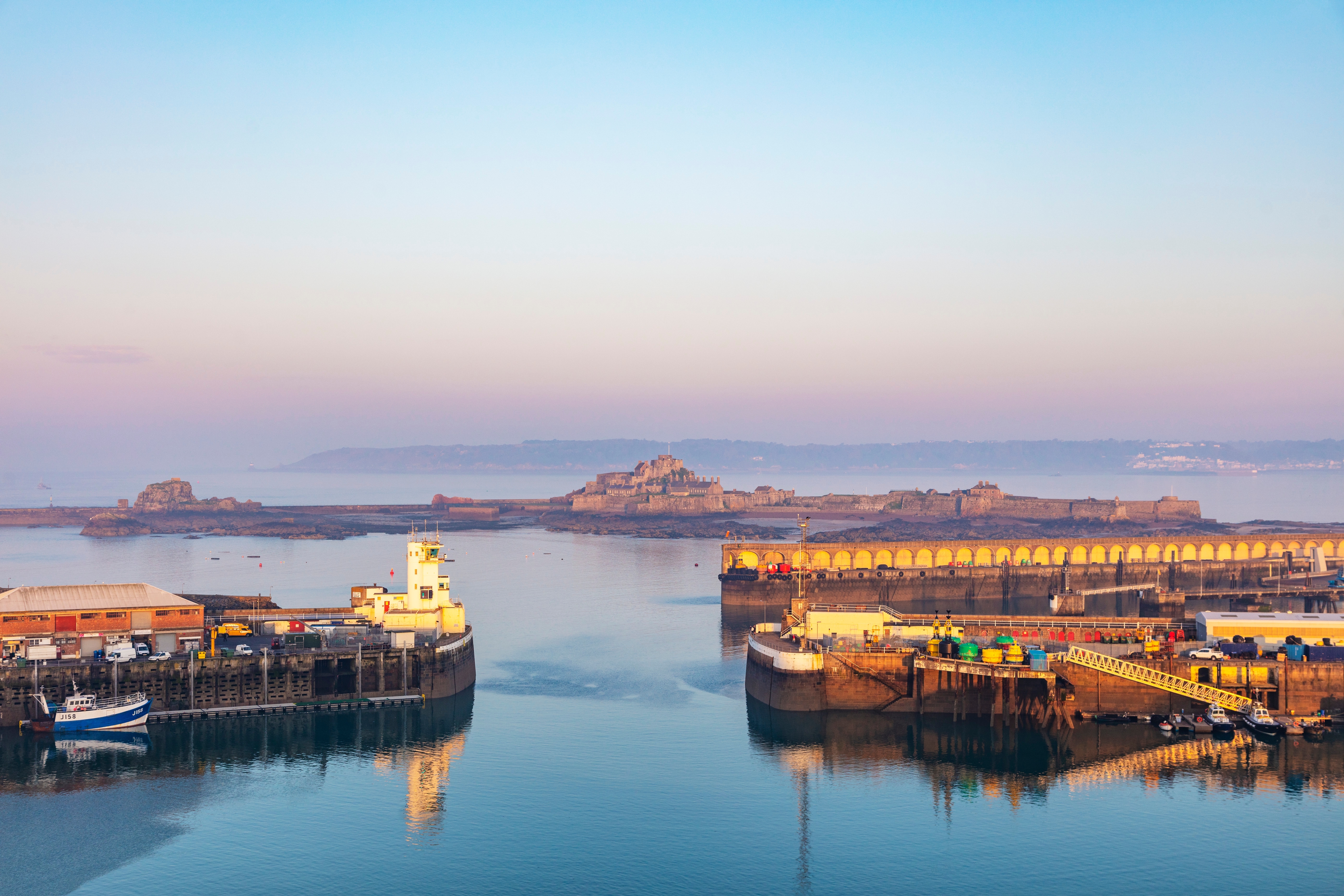 Rolig havn i St. Helier med det historiske Elizabeth Castle i tågen ved solopgang, Jersey