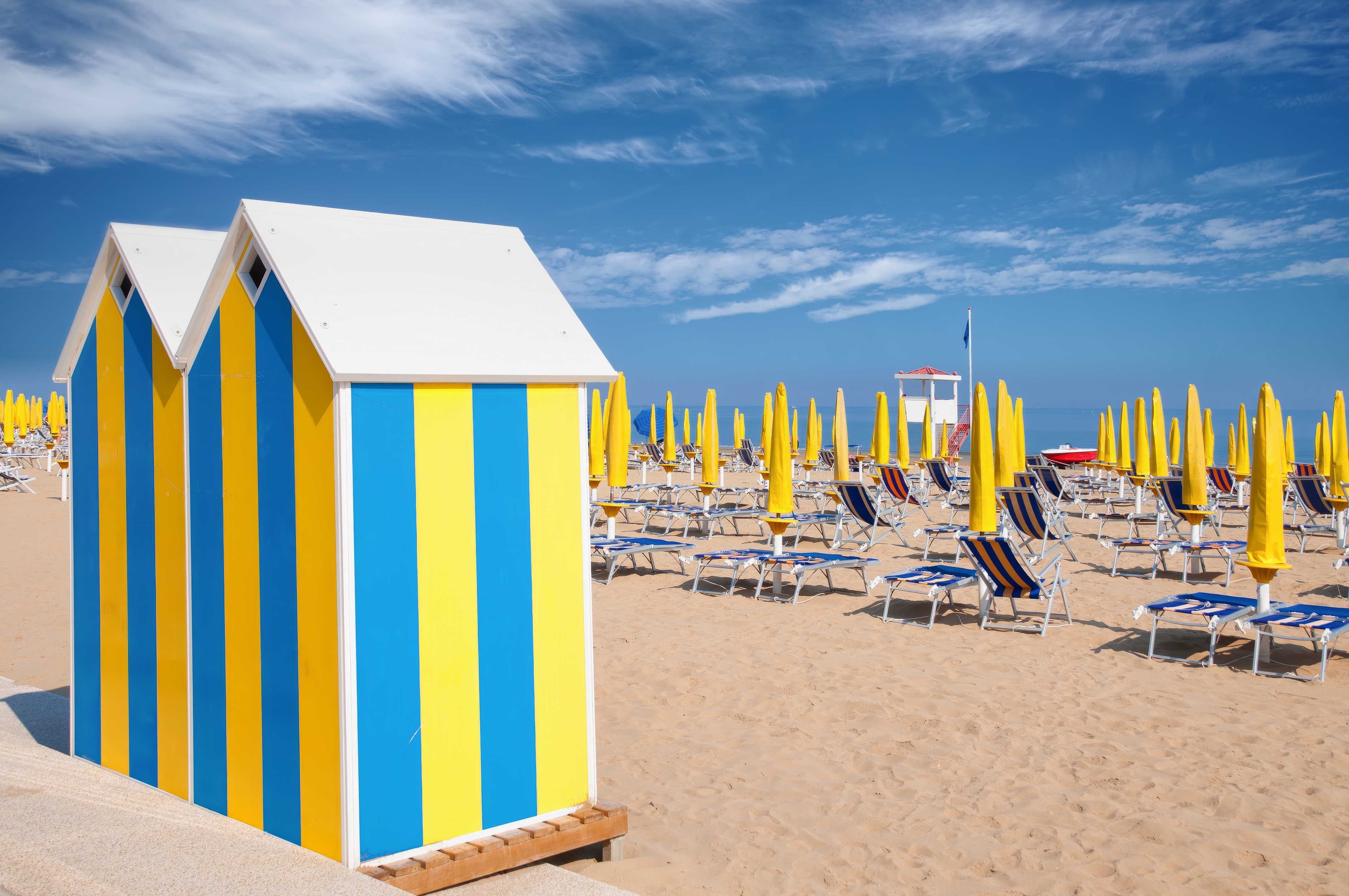 Smuk strandkabine med blå og gule striber omgivet af gule parasoller og liggestole på den brede sandstrand i Lido di Jesolo, Veneto