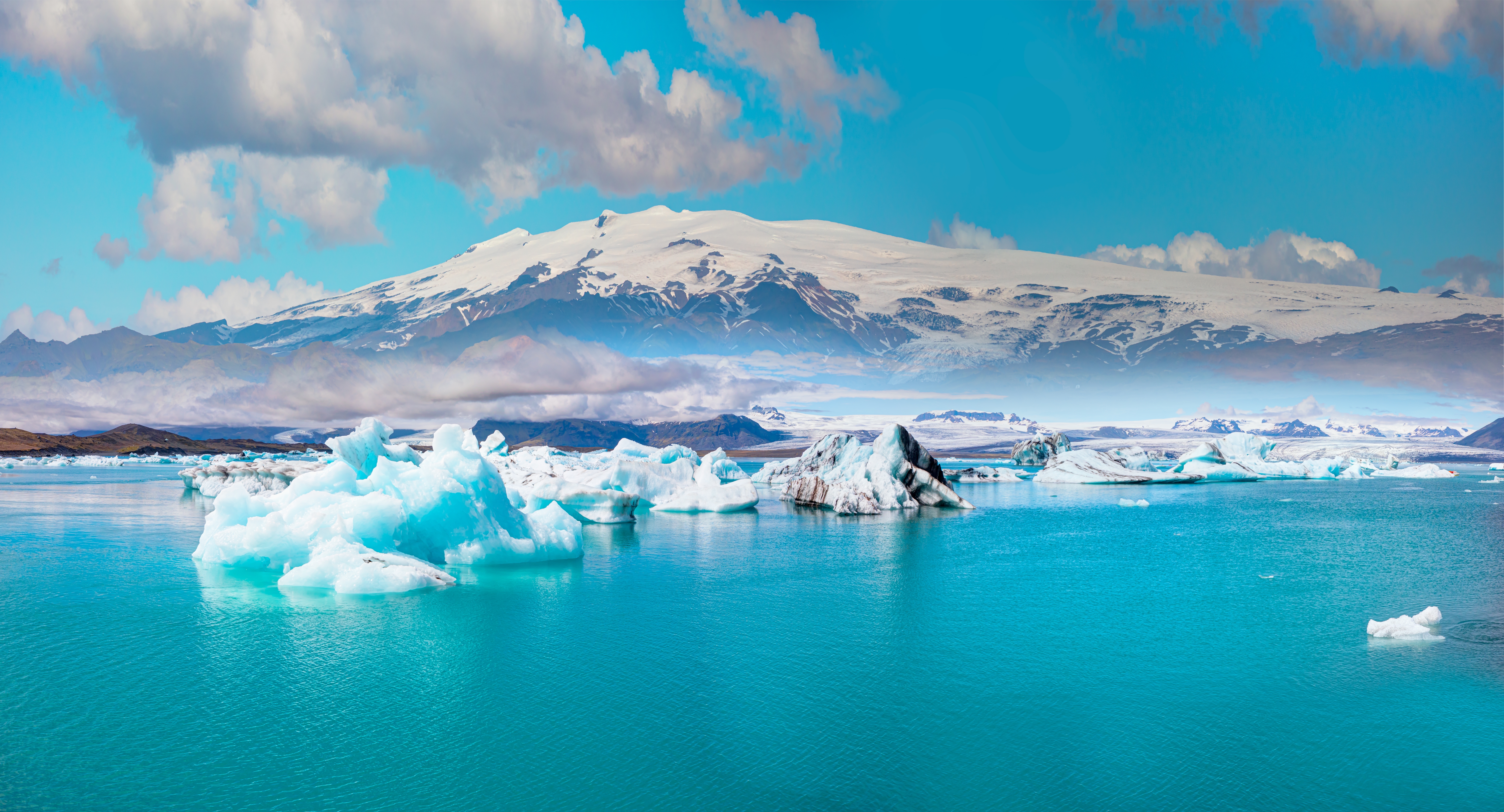 Flydende isbjerge i den isblå Jökulsárlón gletsjersø med snedækket bjerg i baggrunden på Island
