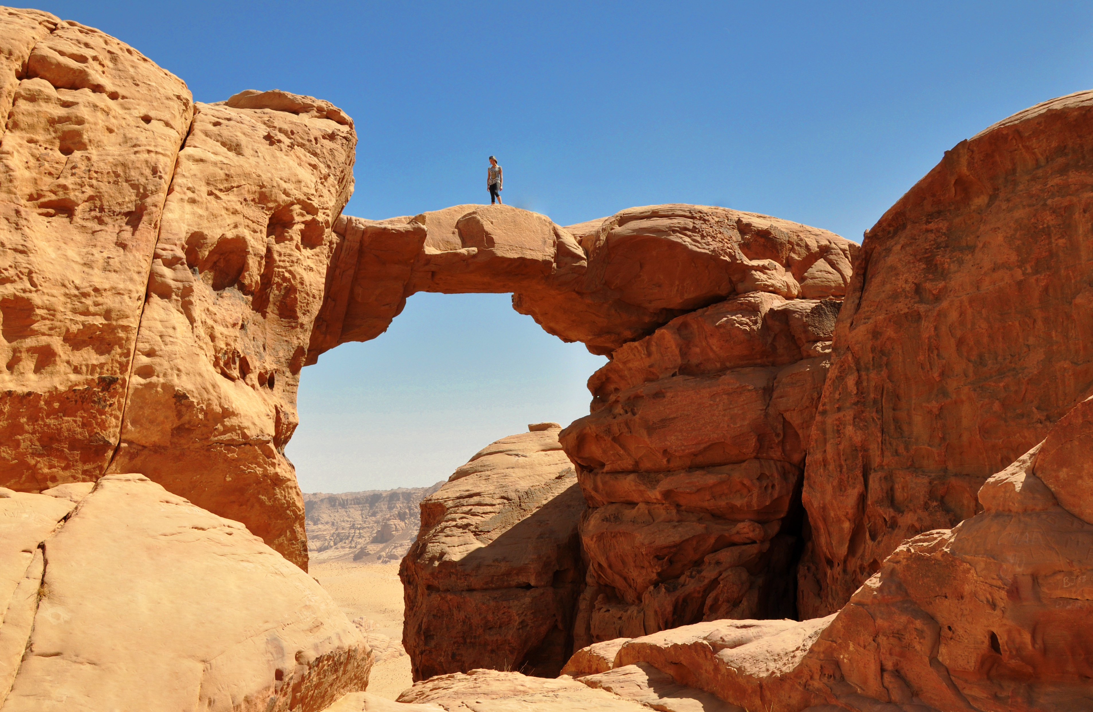 Majestætisk stenbro i den røde Wadi Rum ørken i Jordan med turister der vandrer gennem det dramatiske landskab