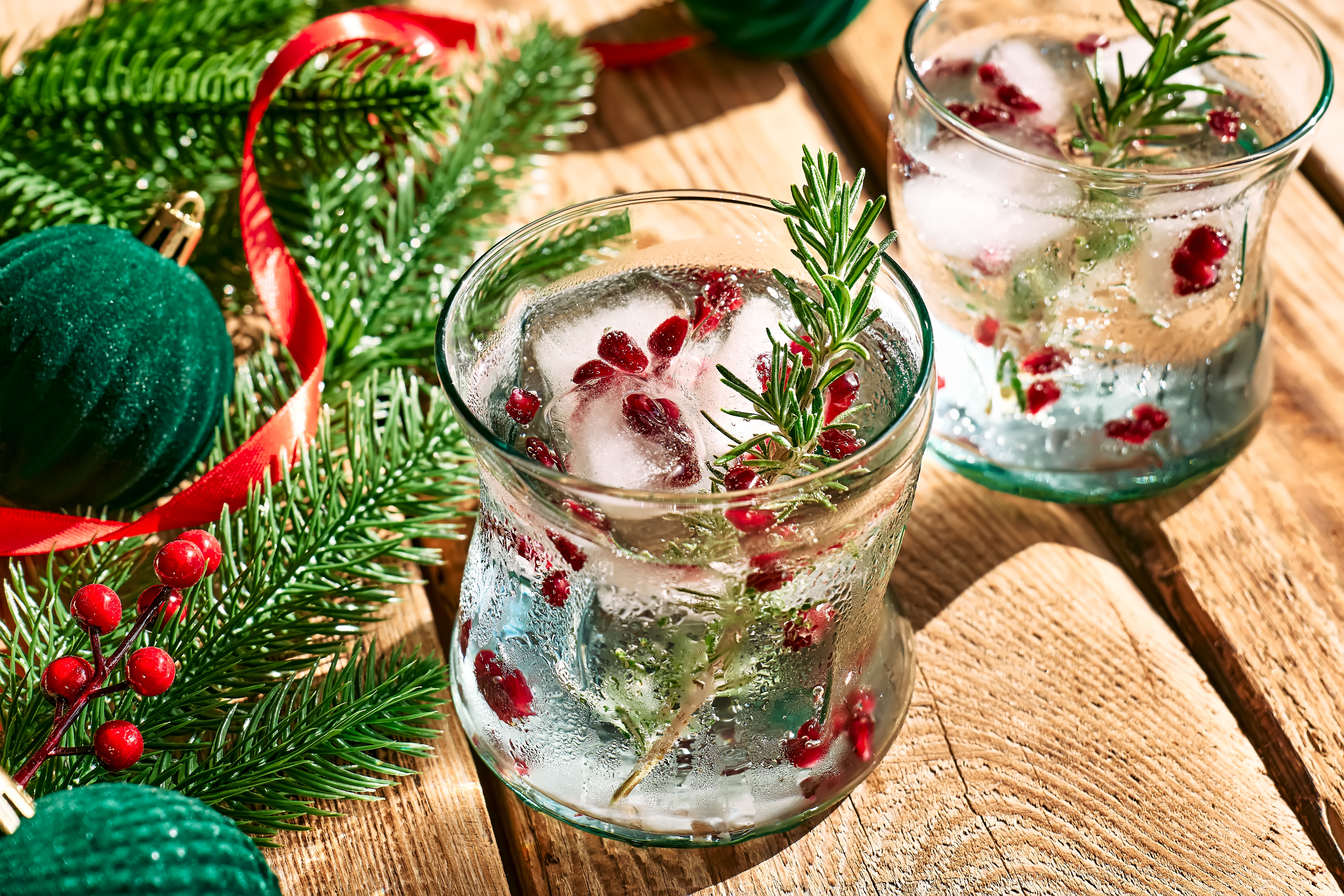 Festlig julcocktail med tranebær, rosmarin og isterninger pyntet med juledekoration på træbord