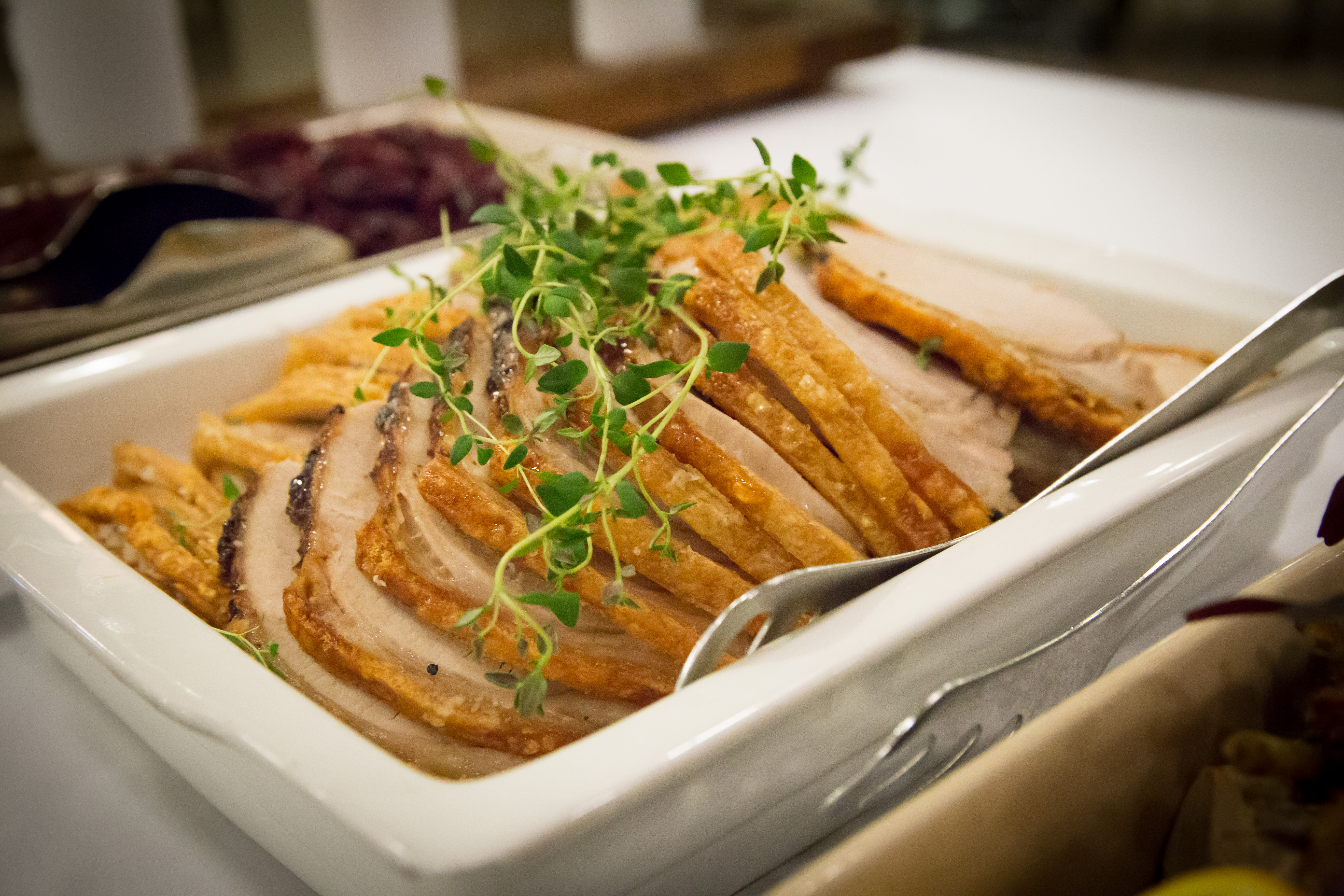 Lækker dansk julefrokost med skiver af flæskesteg og sprød svær dekoreret med frisk timian i hvid skål