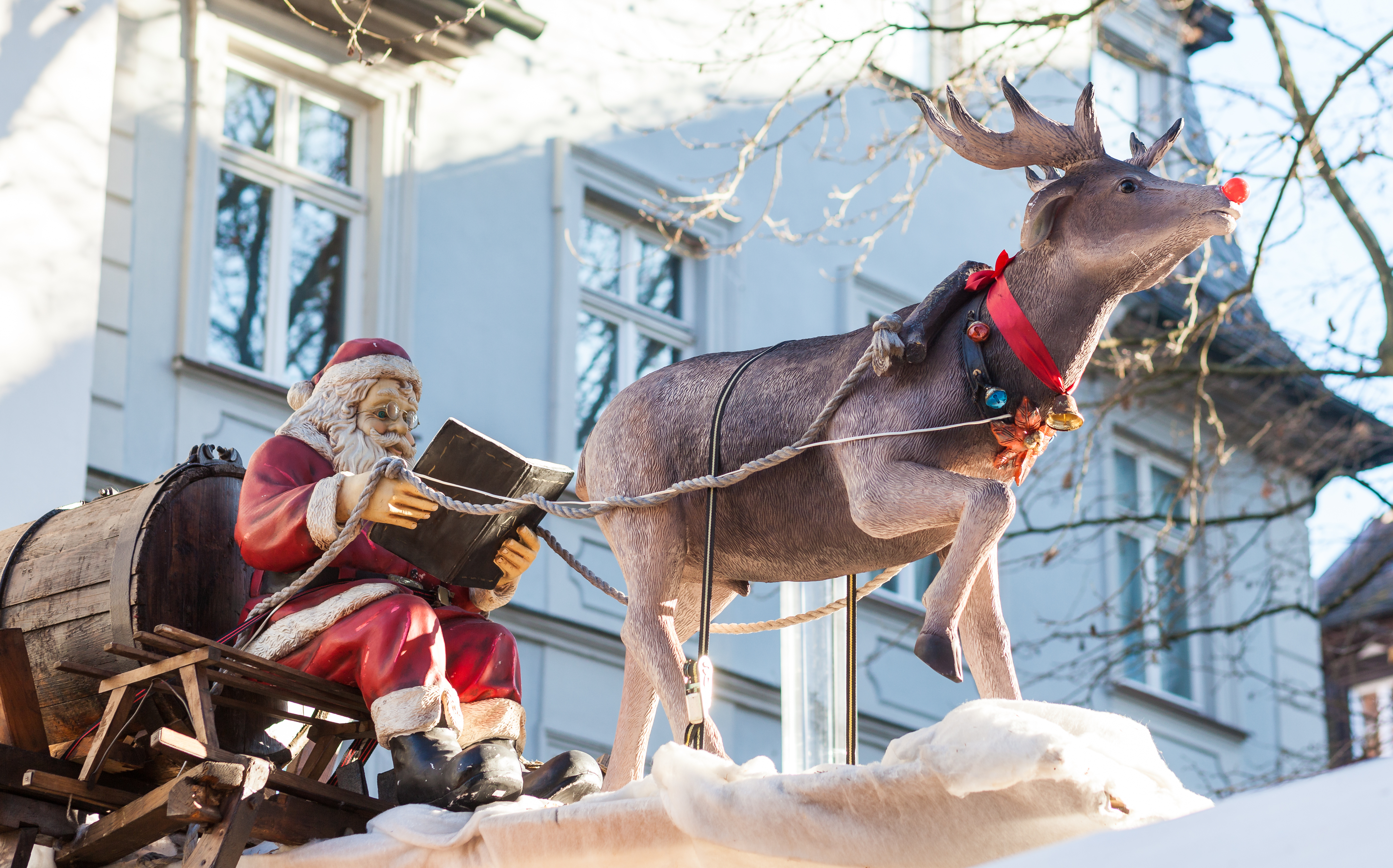 Julemand læser bog til rensdyr i snedækket juleby under vinterferie