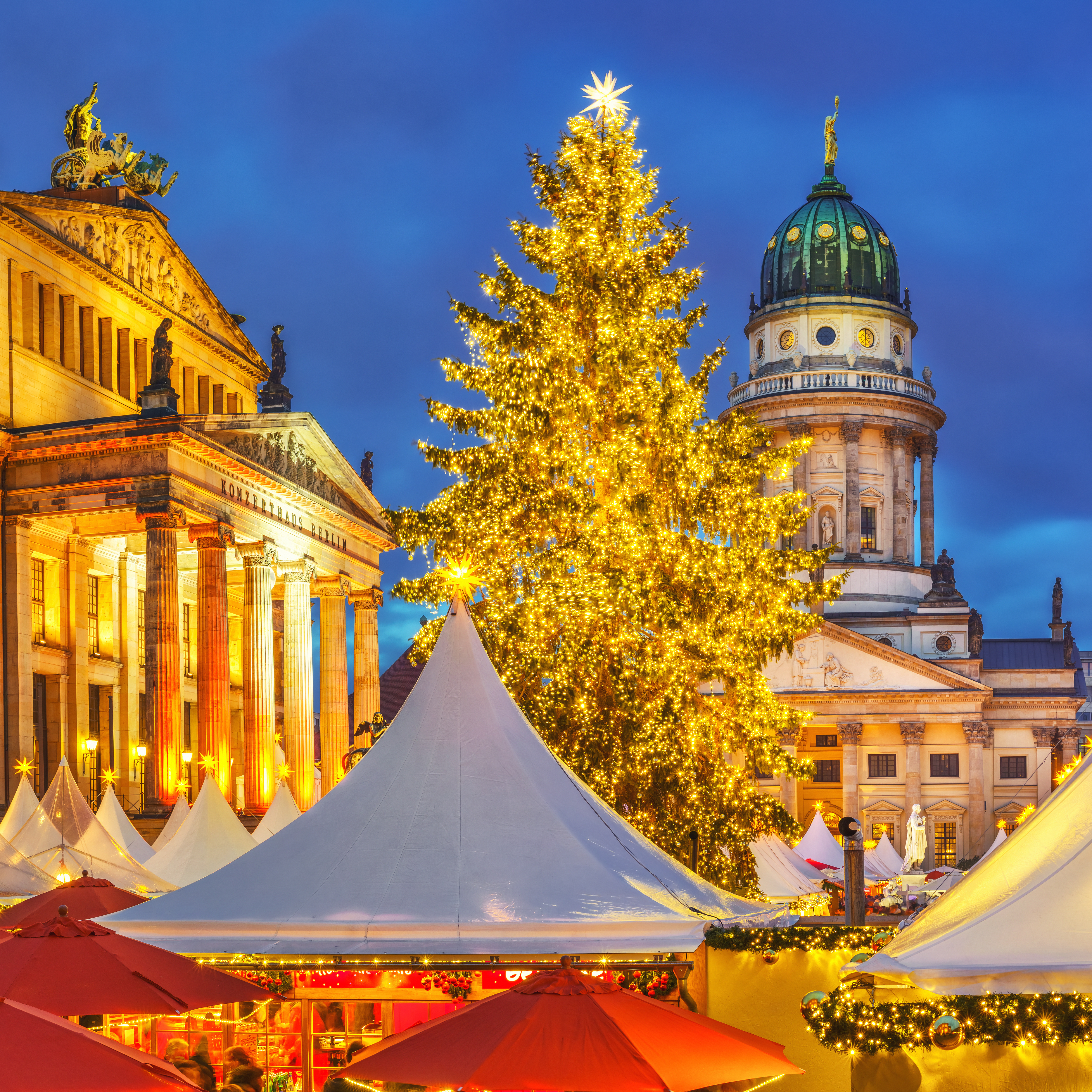 Julemarked i Berlin med oplyst katedral og gyldent juletræ i aftenlys