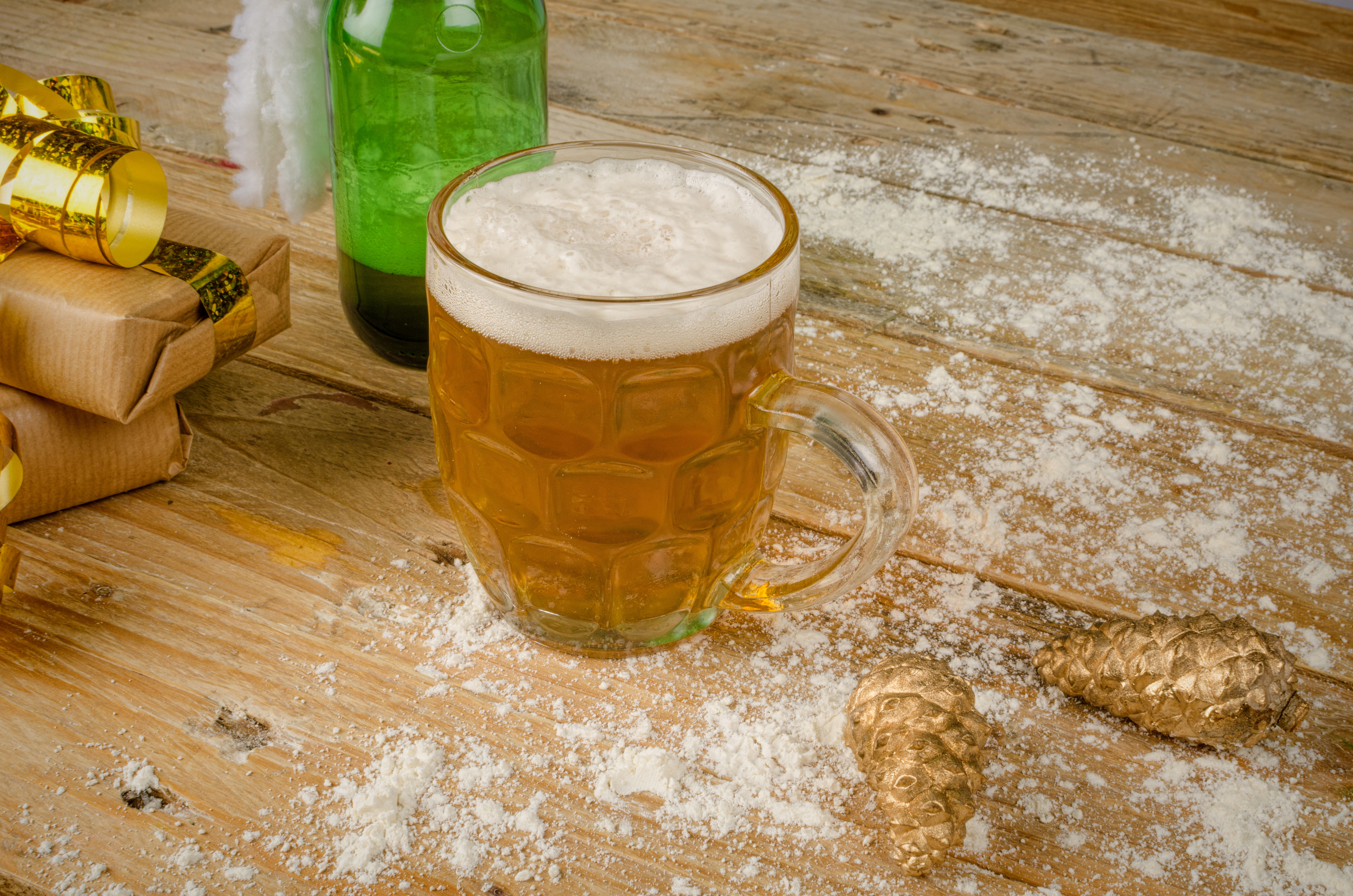 Traditionelt dansk julebryg serveret i klart ølkrus med skum, omgivet af julepynt og kunstig sne