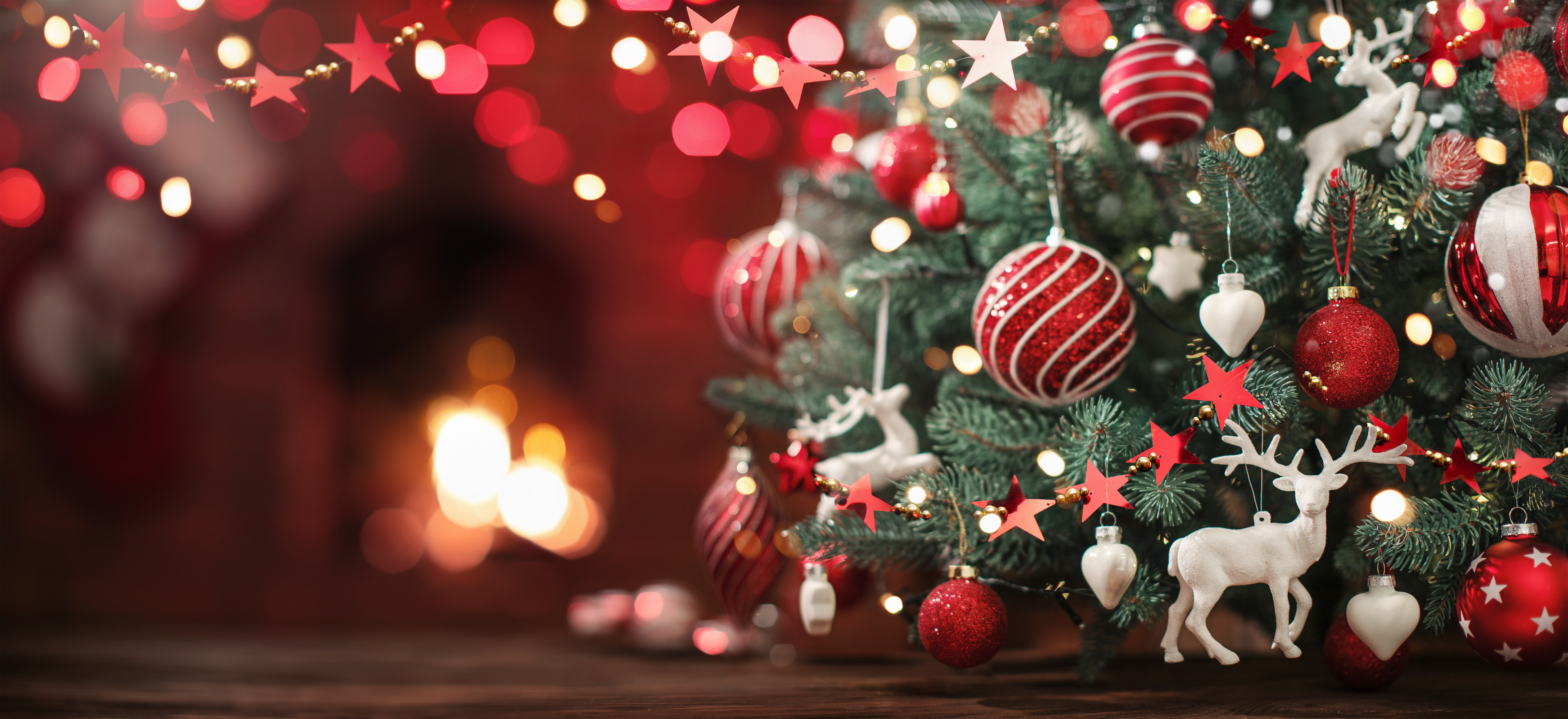 Hyggeligt juletræ med røde julekugler, hvide rensdyrsfigurer og twinkling lys ved en varm pejs i julestemning