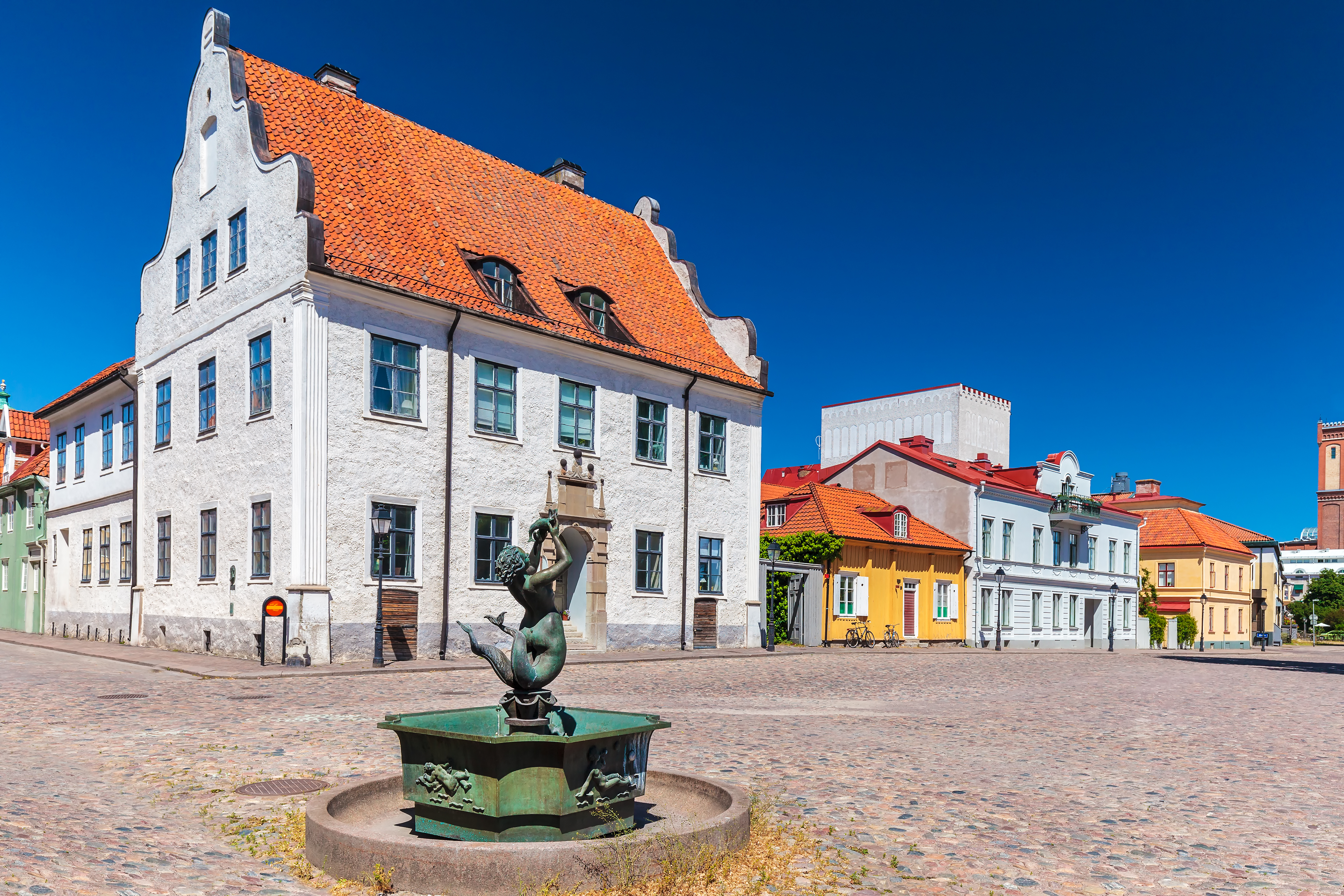 Smukt brolagt torv i Kalmar med en dekorativ bronzefontæne og velbevarede historiske bygninger med orange tegltage i Sverige