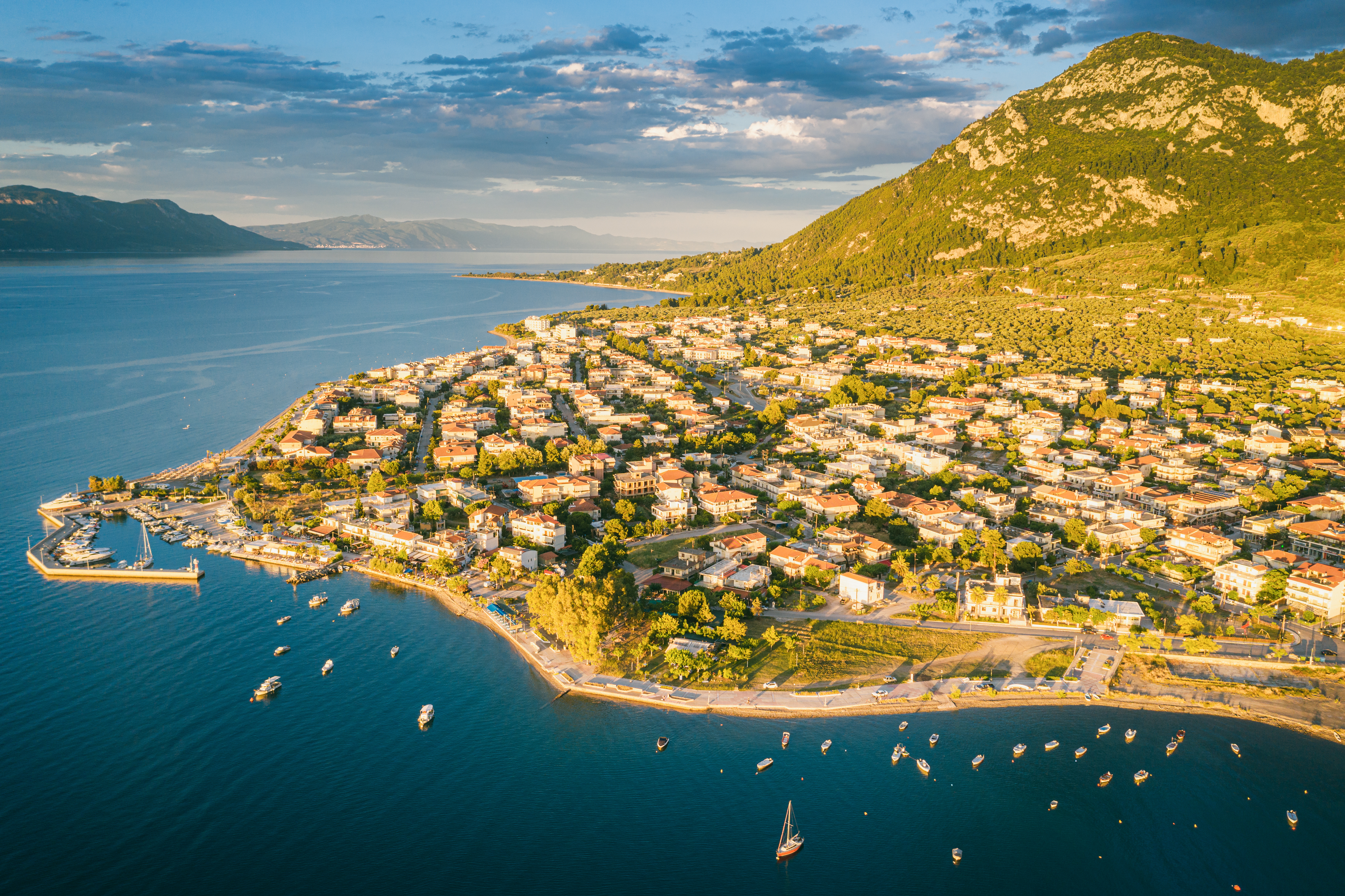 Dronefoto af Kamena Vourla i Grækenland med azurblåt middelhav, marina og grønne bjerge under blå himmel