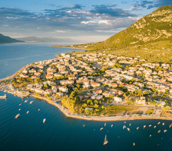 Dronefoto af Kamena Vourla i Grækenland med azurblåt middelhav, marina og grønne bjerge under blå himmel