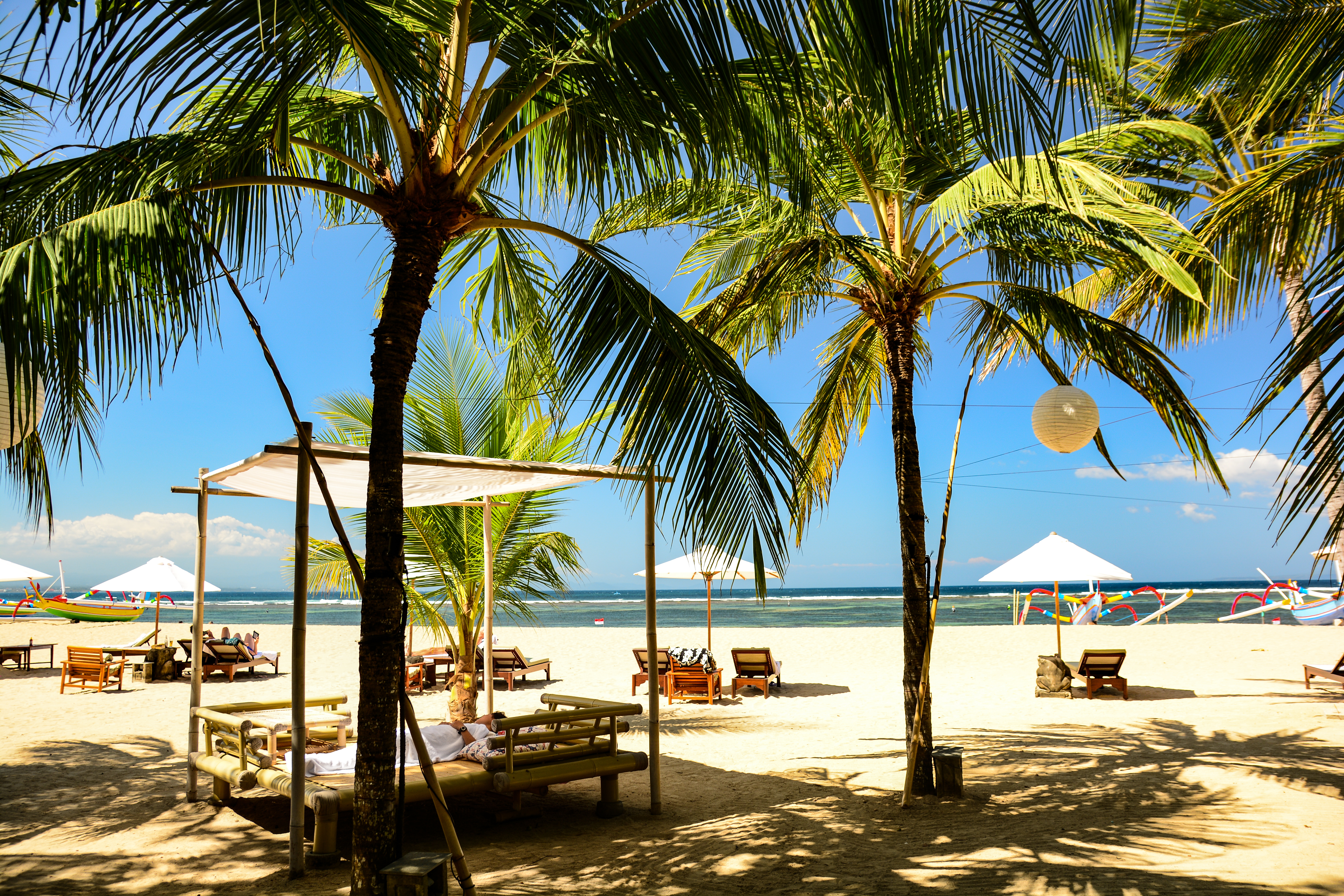 Fredfyldt tropisk strand med vippende palmtræer og blåt hav ved Karang Beach i Sanur, Bali
