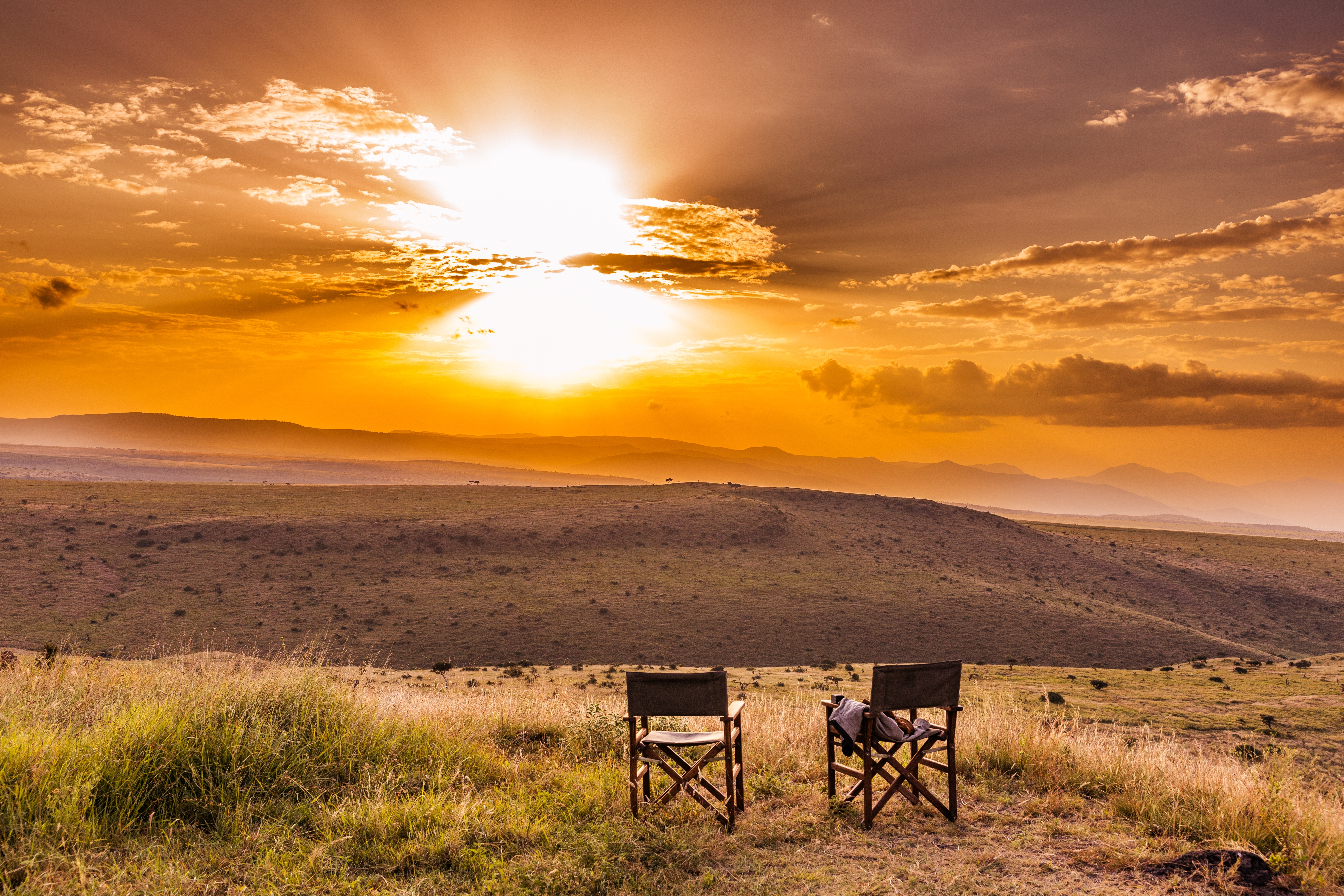 Betagende solnedgang over den afrikanske savanne med to stole placeret for at nyde udsigten i Lewa Wildlife Conservancy, Kenya.