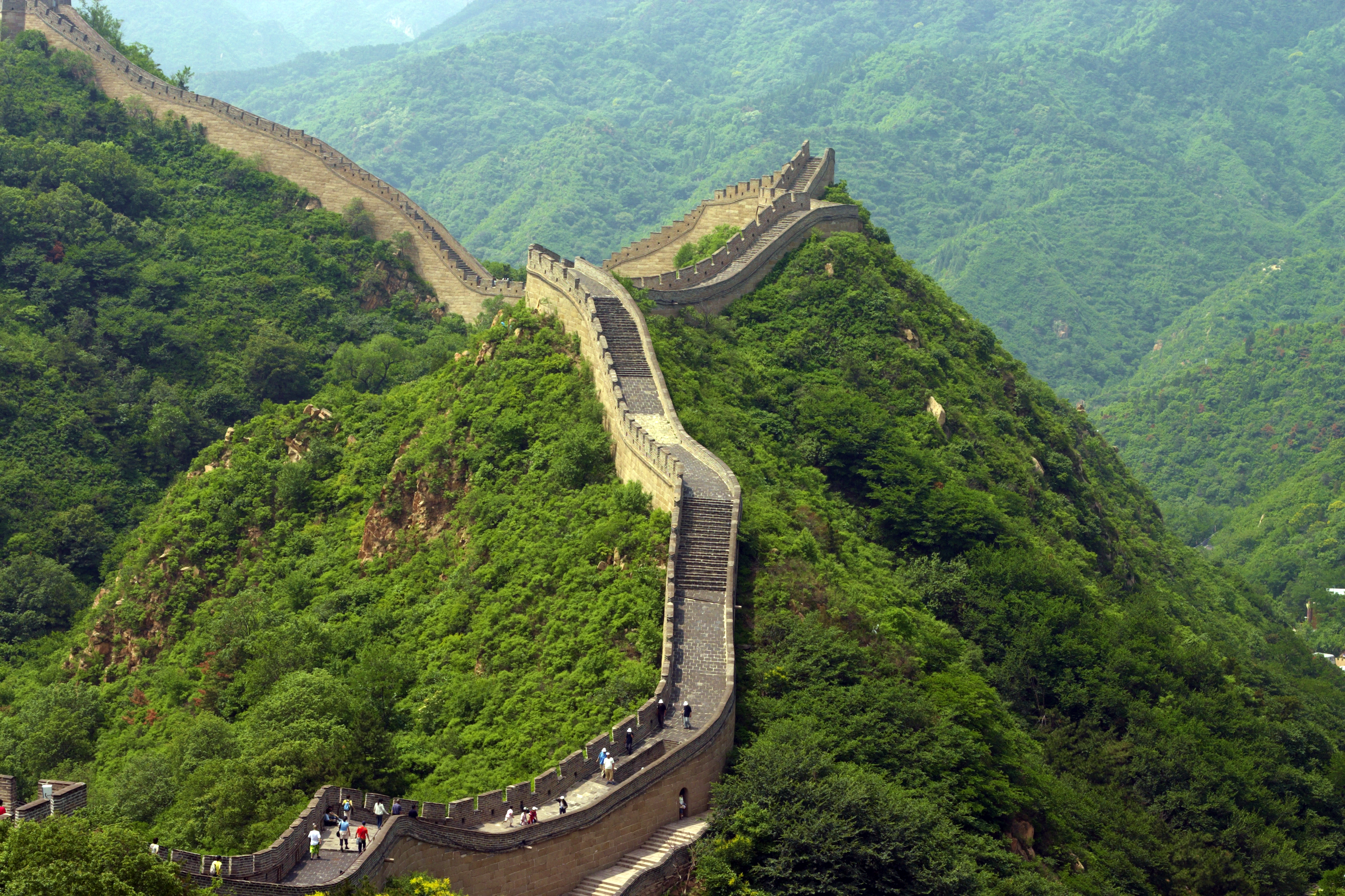 Storslået udsigt over Den Kinesiske Mur, der snor sig gennem det grønne bjerglandskab nær Beijing - en fascinerende historisk seværdighed og et af verdens vidundere