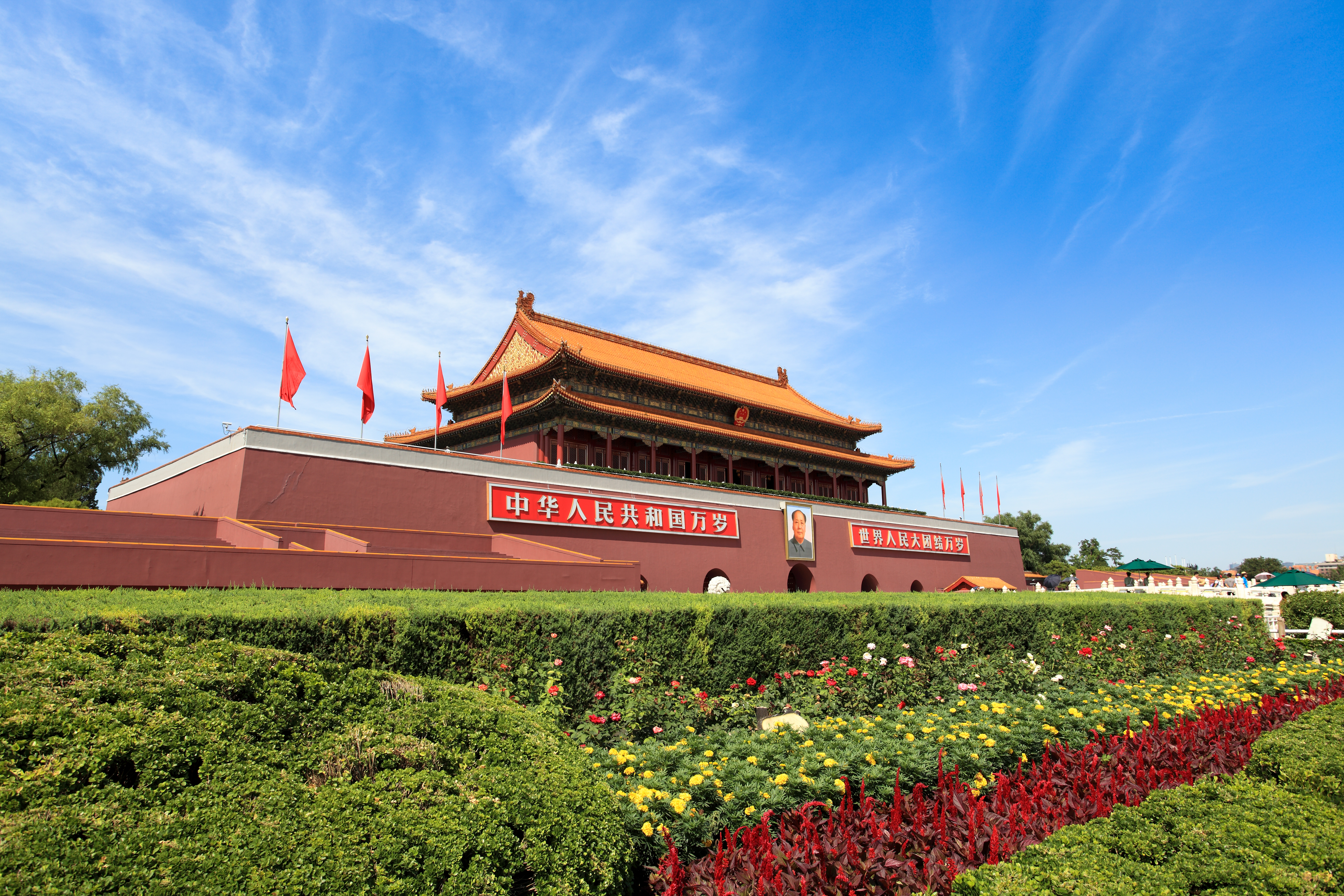 Tiananmen-porten i Beijing, Kina, med den karakteristiske røde facade, kinesiske flag og storslåede kejserlige arkitektur omgivet af grønne haver