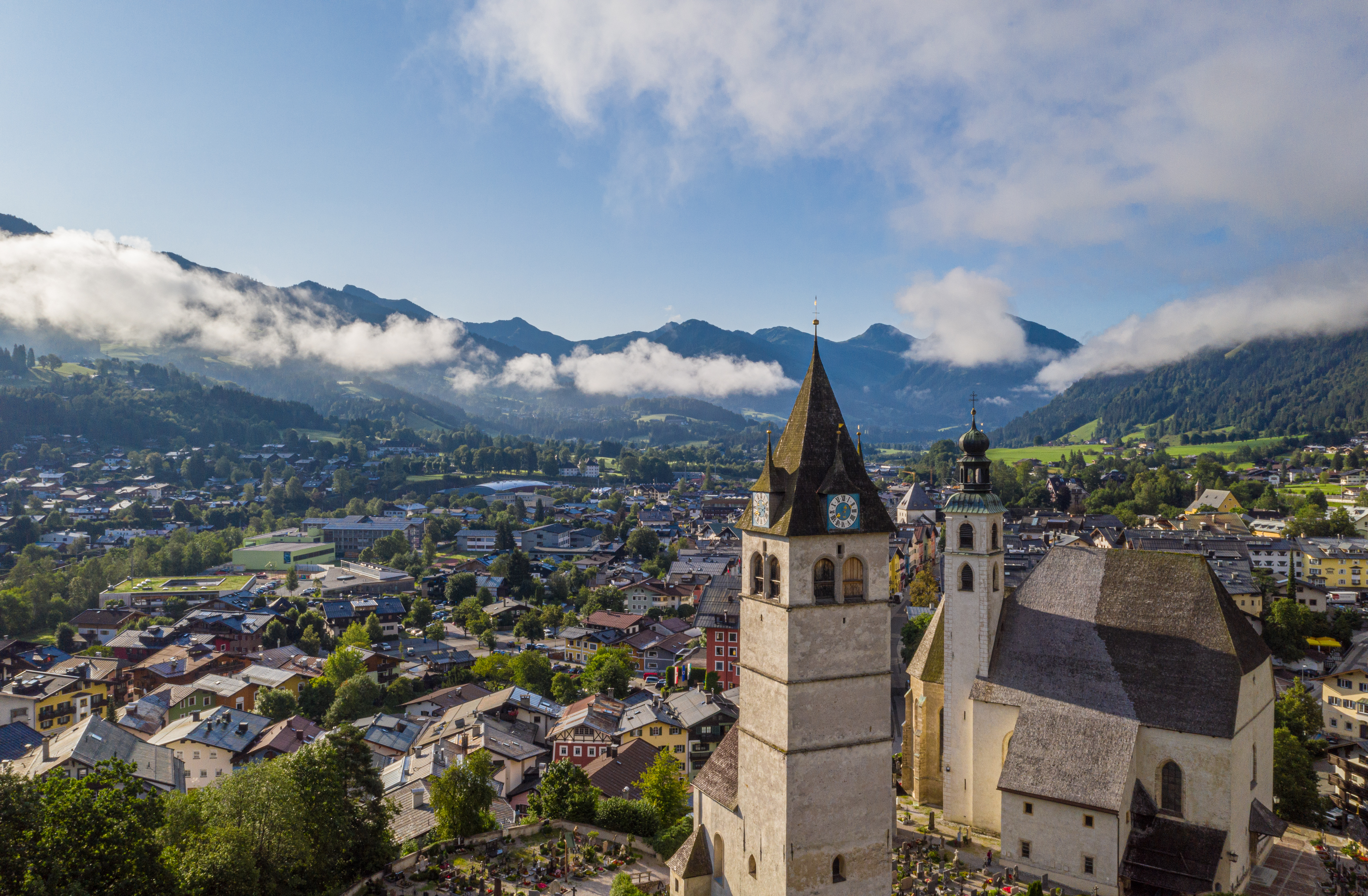 Malerisk fugleperspektiv over Kitzbühel med historiske kirketårne og klassisk østrigsk alpelandsby omgivet af bjerge i Tyrol