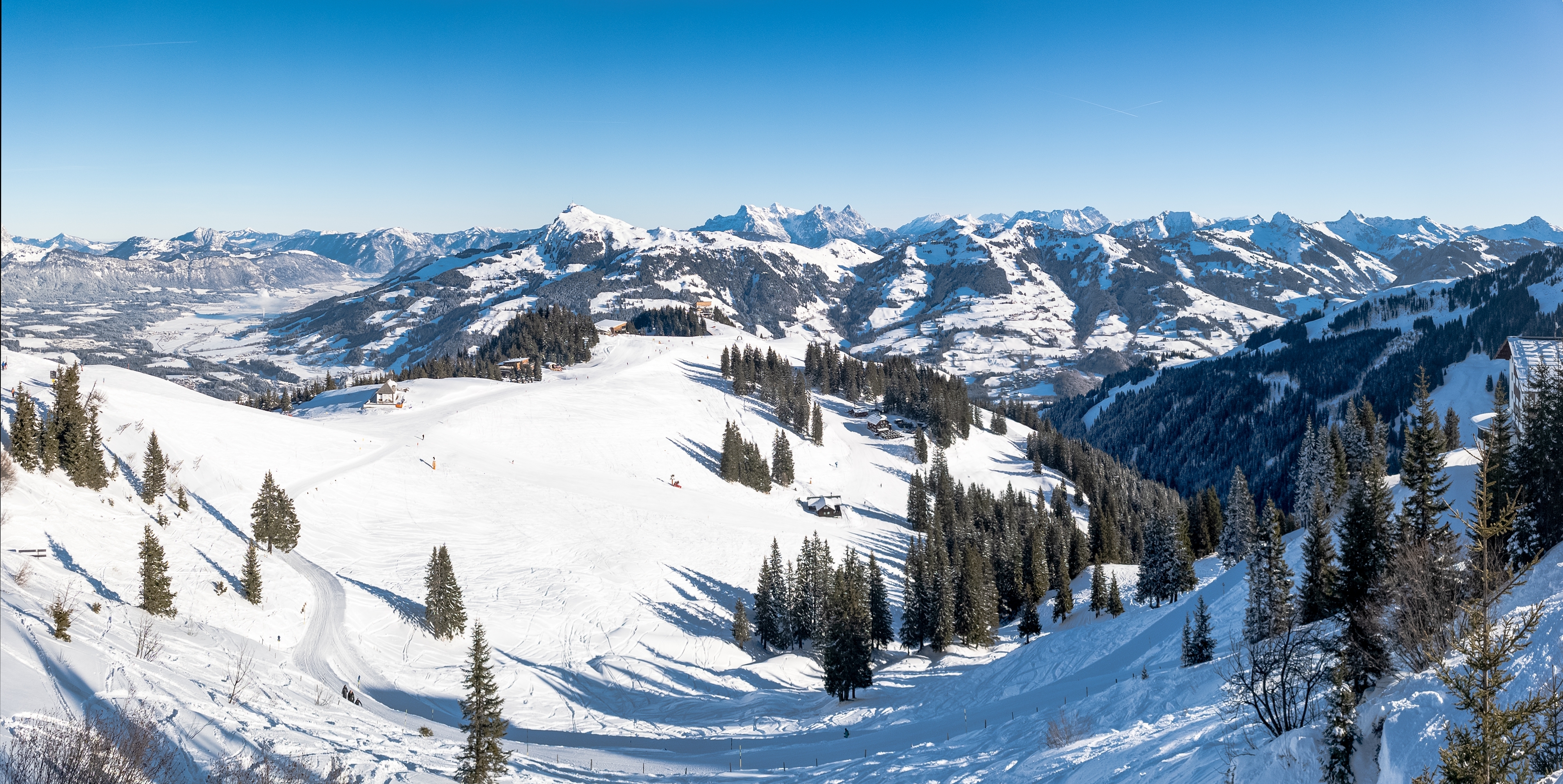 Smuk vinterpanorama fra Kitzbühel i Tyrol med snedækkede alpepister, tæt nåleskov og majestætiske bjergtinder i Østrig