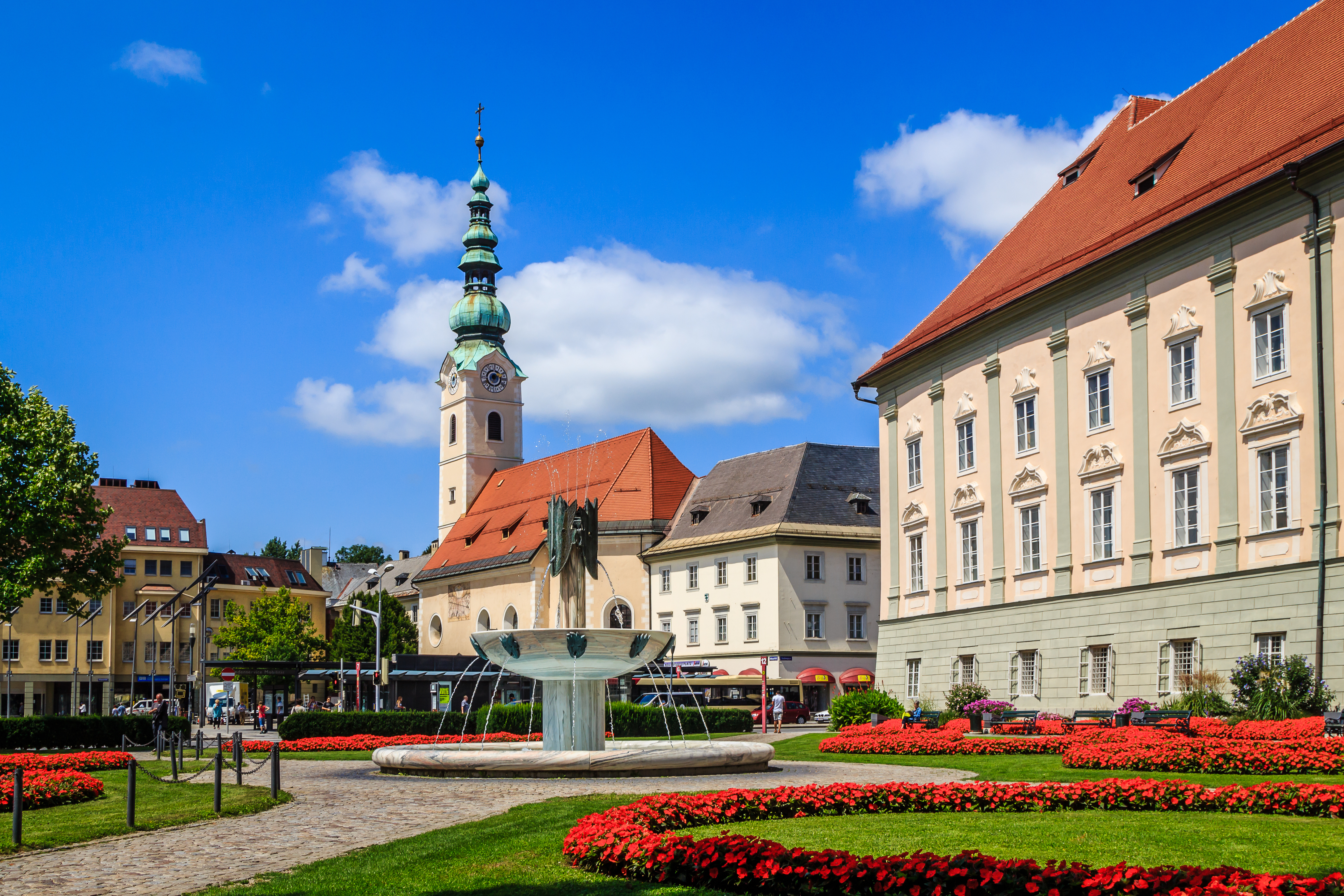 Imponerende arkitektur i Klagenfurt med Landhaus bygningen, Kiki-Kogelnik springvandet og kirketårn under blå himmel i Kärnten, Østrig