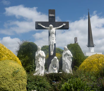 Smukke hvide marmorstatuer ved Knock Shrine i Irland forestiller korsfæstelsen med Jomfru Maria og helgener, omgivet af gyldne topiarbuskadser og en kirkespir