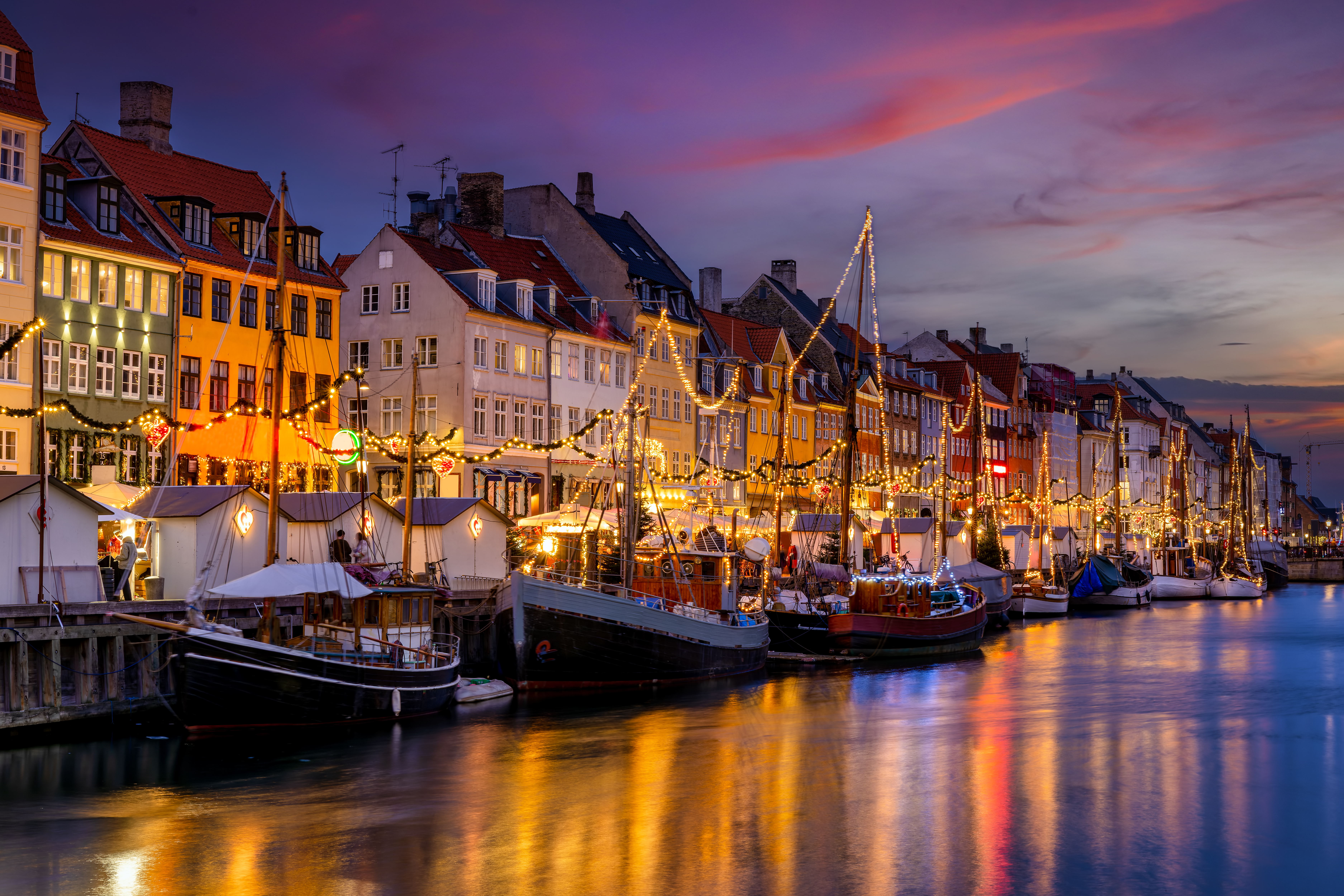 Stemningsfuld juleudflugt til Nyhavn i København med festlige lysdekorationer på både og historiske bygninger ved smuk vintersonedgang