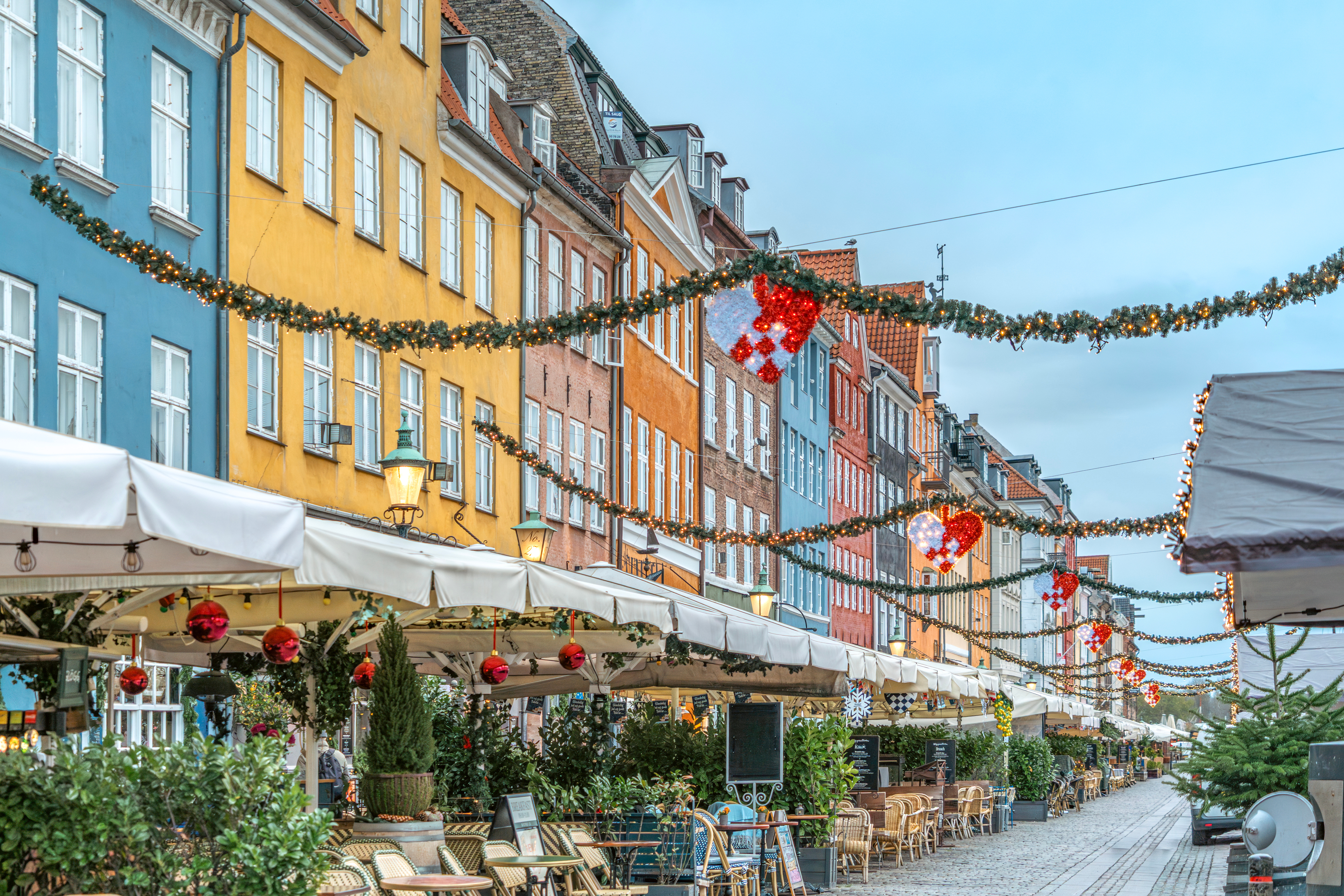 Julestemt Nyhavn i København med farverige historiske facader, julegirlandere og hyggelige restaurantterrasser