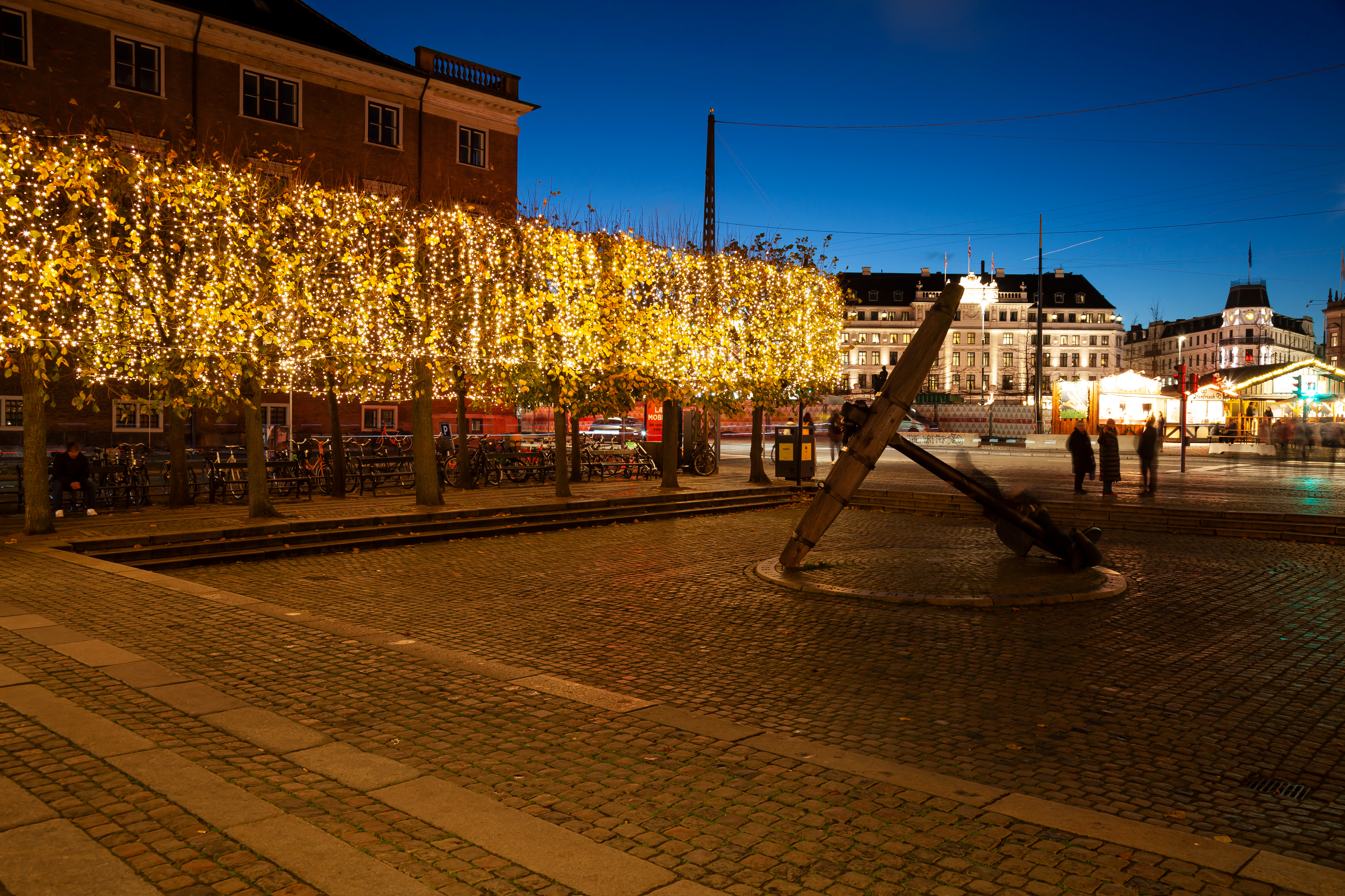 Magisk julestimning ved Nyhavn i København med guldlyse træer og historisk anker på brosten om aftenen