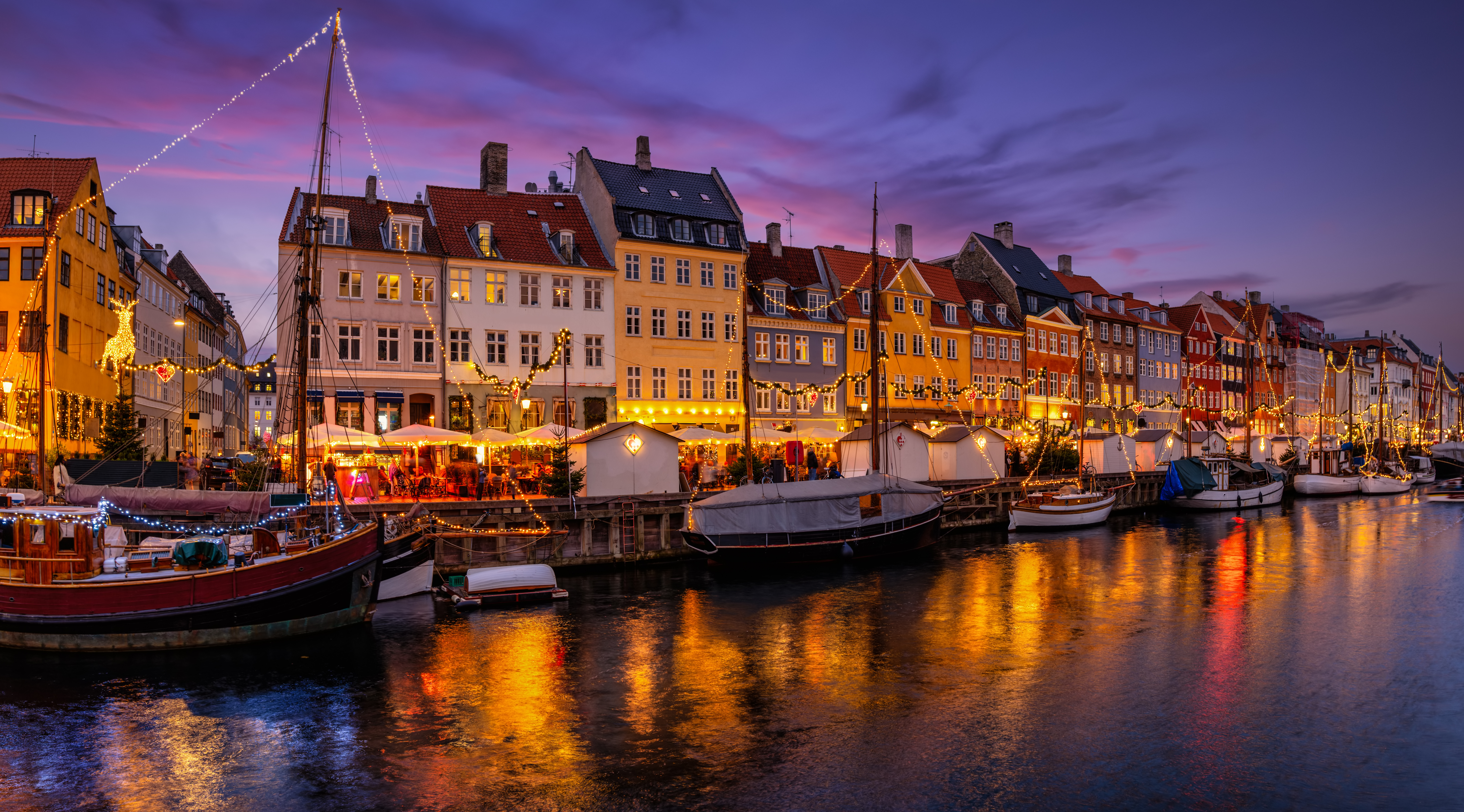 Julestemning ved Nyhavn i København med smukke farverige bygninger, lysdekorationer og både langs kanalen i den romantiske aftenstemning