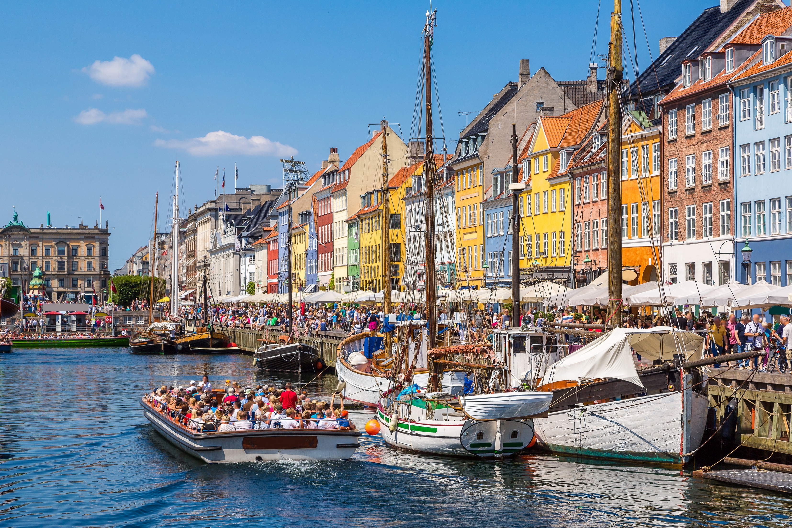 Turistbåde og historiske sejlskibe i den maleriske Nyhavn på en solrig dag i København