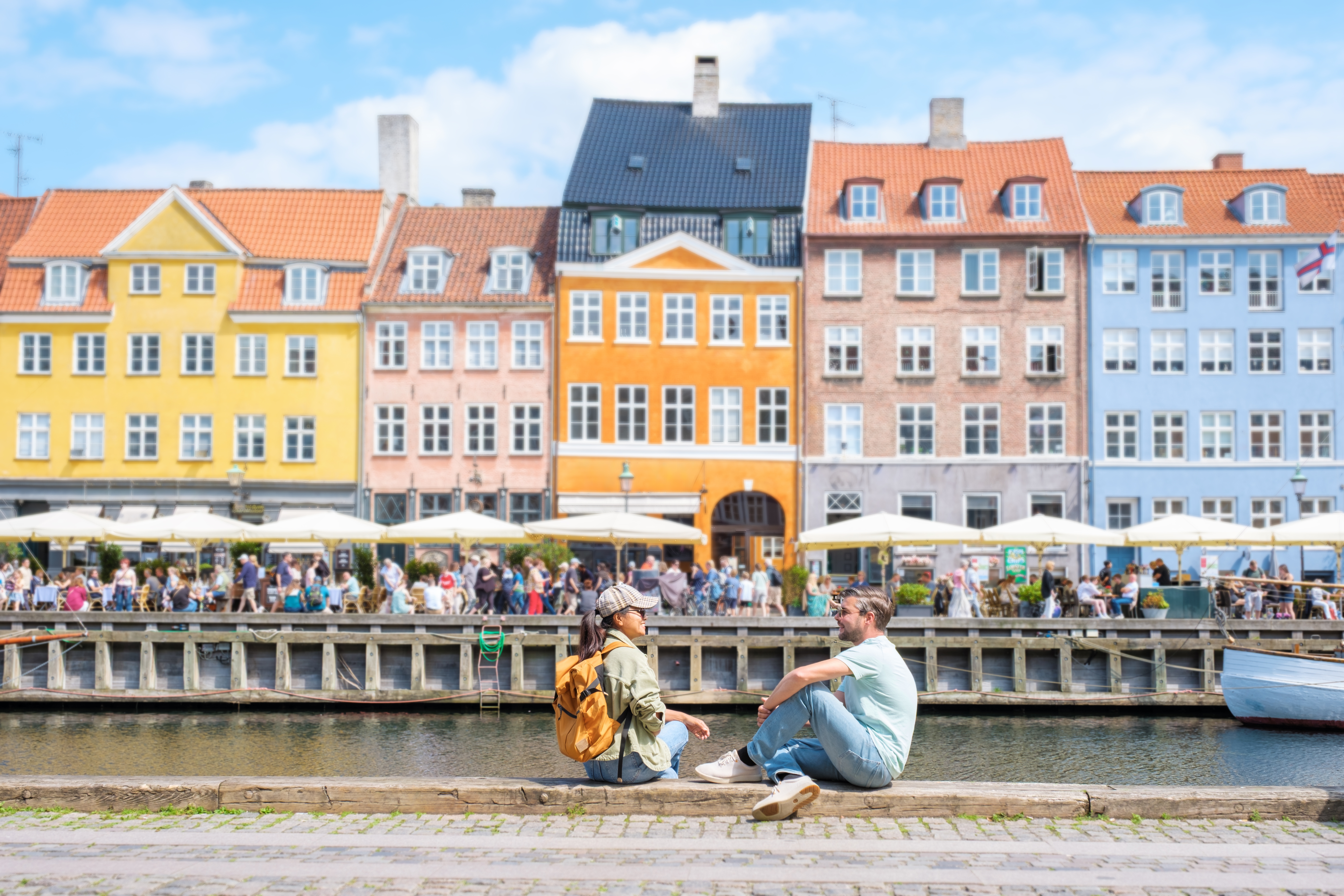 Turister nyder det dejlige sommervejr ved Nyhavn i København med smukke farverige bygninger og restauranter langs den historiske kanal