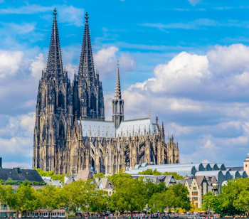 Köln Domkirkes imponerende gotiske facade med to høje spir fotograferet fra Rhinen på en skyfri sommerdag