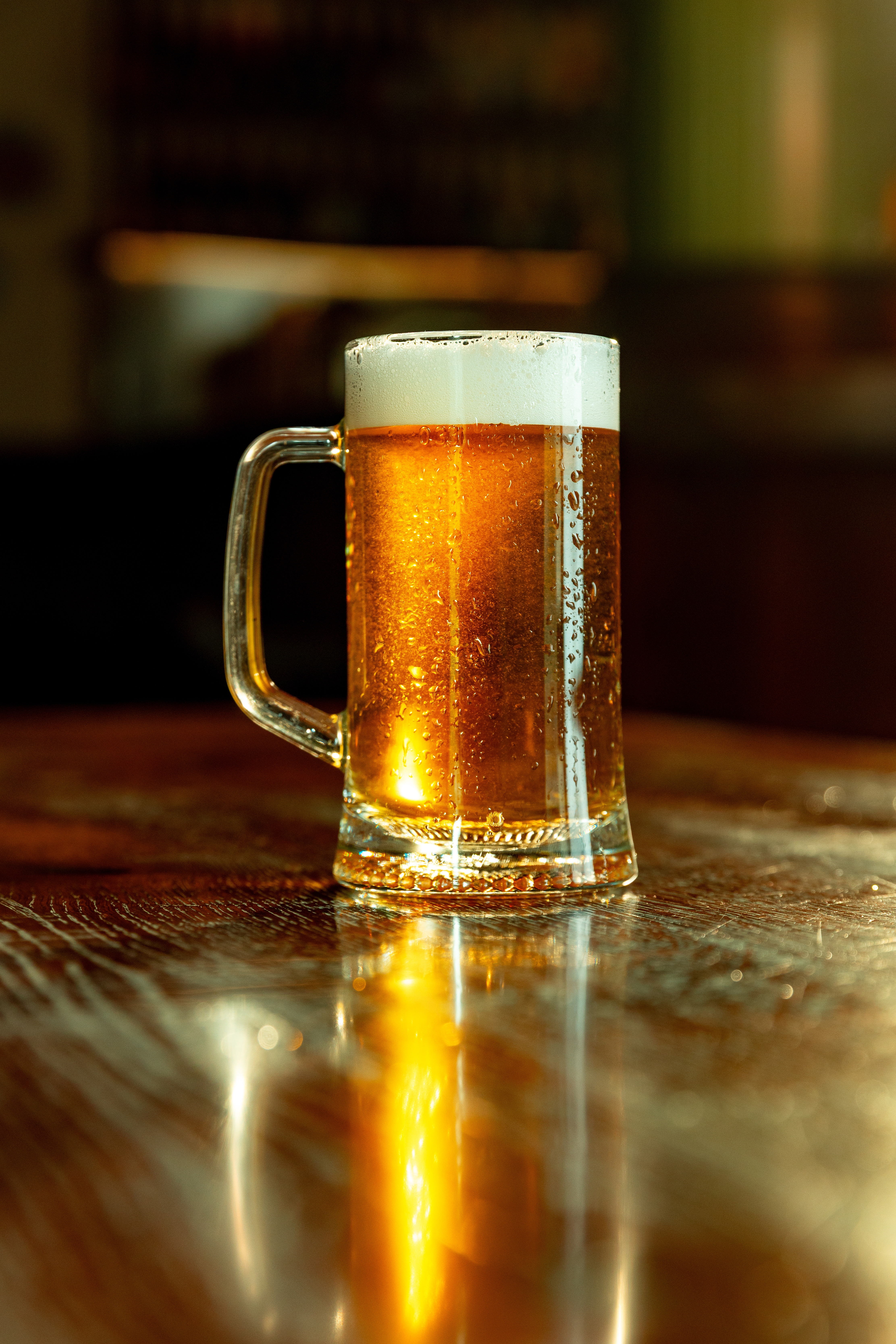 Frostkoldt ølkrus med gyldent øl og tyk skumkrone på blank bardisk i stemningsfuld pub til Oktoberfest