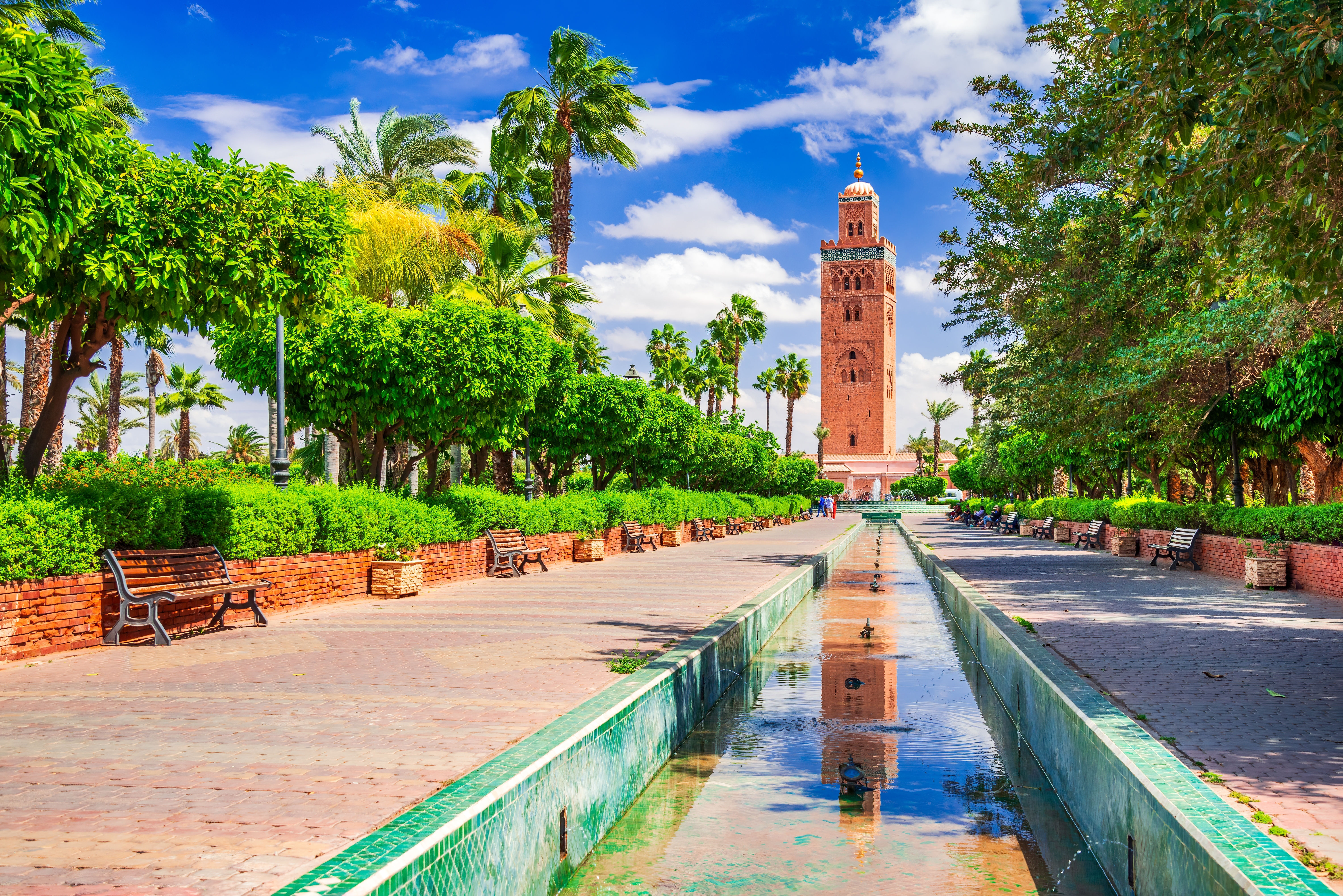 Koutoubia Moské tårn med islamisk arkitektur i Marrakech omgivet af tropiske palmer og reflekterende vandbassin