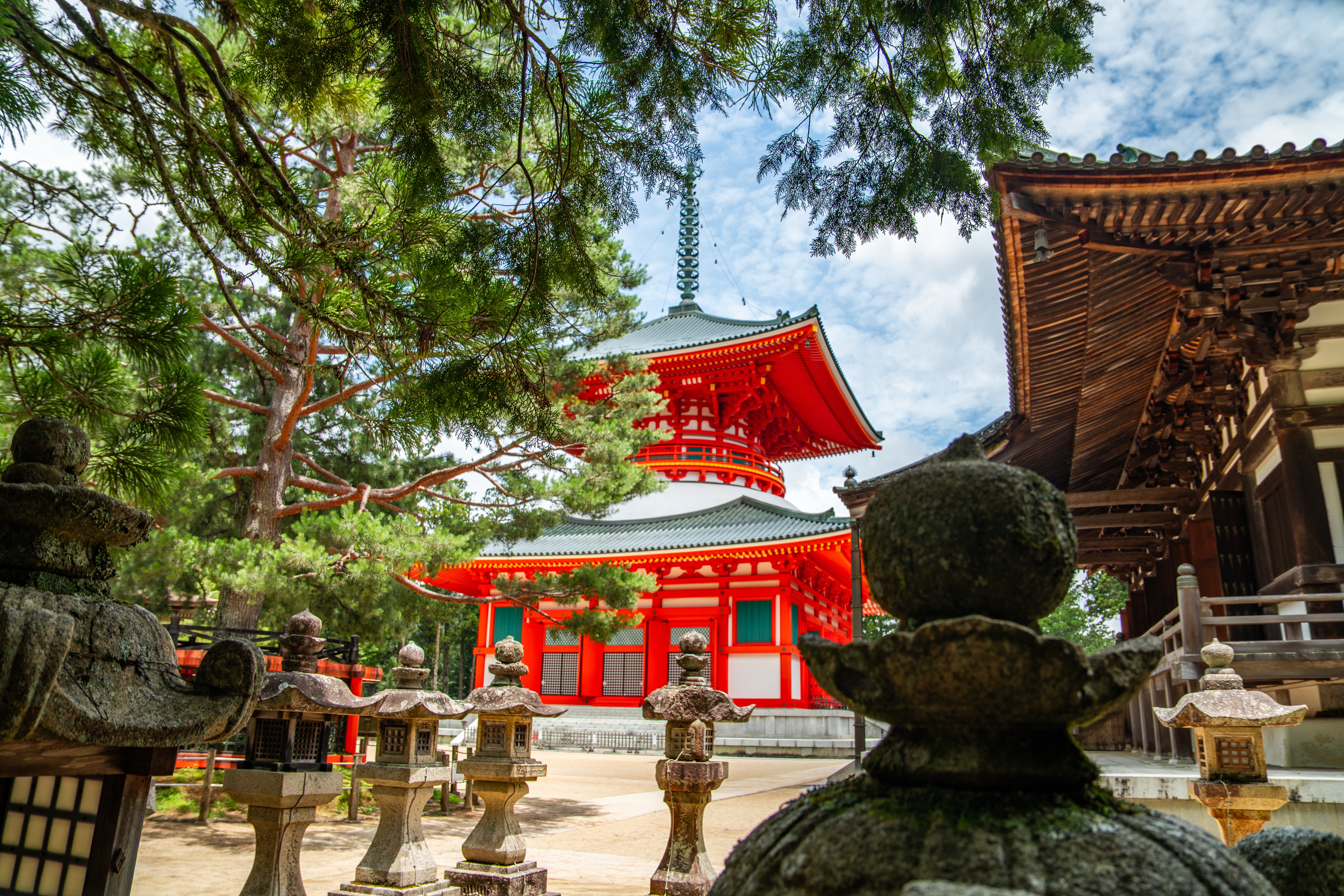 Buddhistisk tempel med ikonisk rød pagoda i Koyasan, Wakayama, Japan, flankeret af stenlanterneR og grønne træer